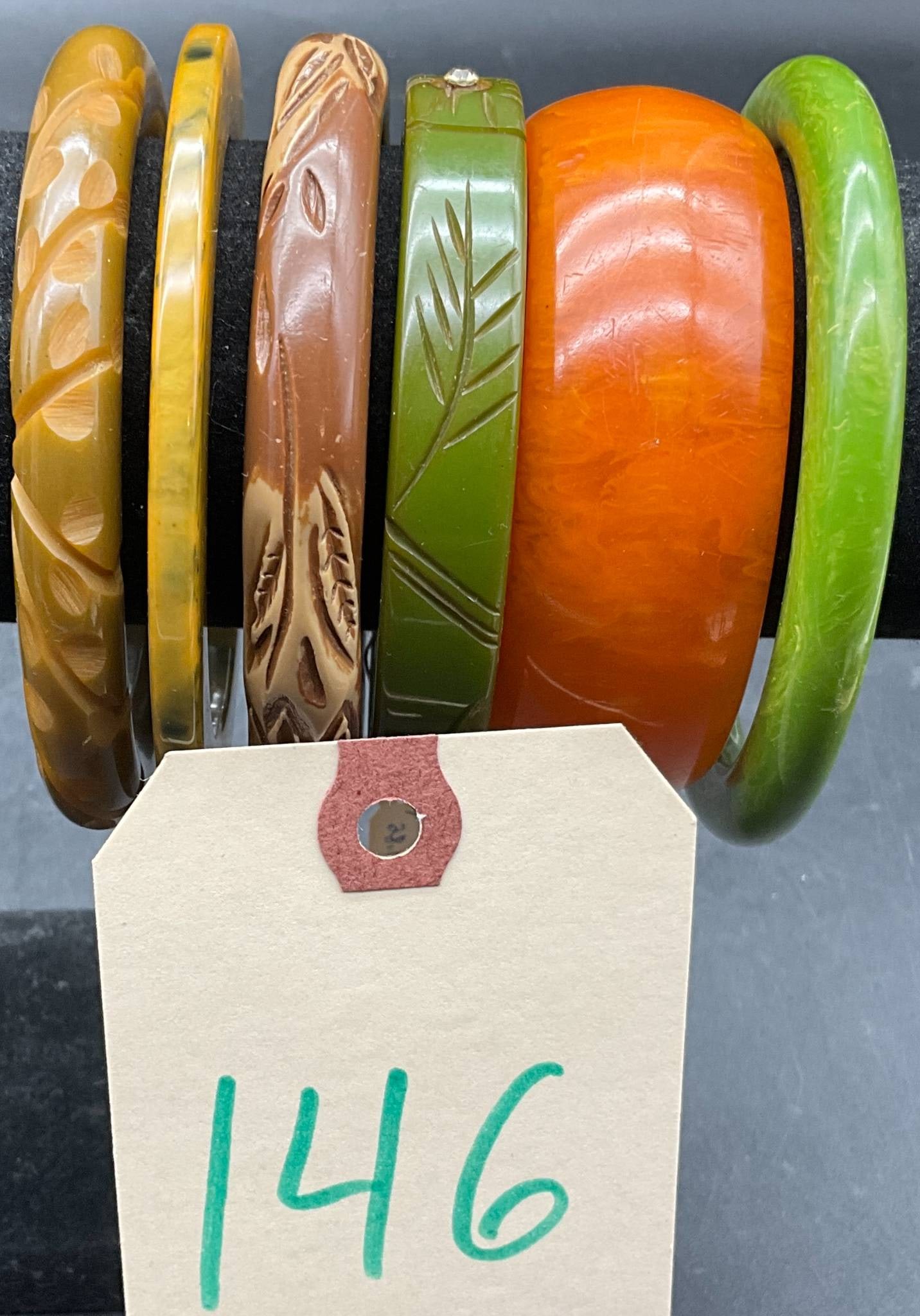 Vintage Carved and Smooth Bakelite Bangles: Six vintage bakelite bangles featuring a mix of carved and smooth designs. Includes pieces in green, orange, brown, and yellow hues. Carved examples showcase leaf and floral motifs, with one bangle ac