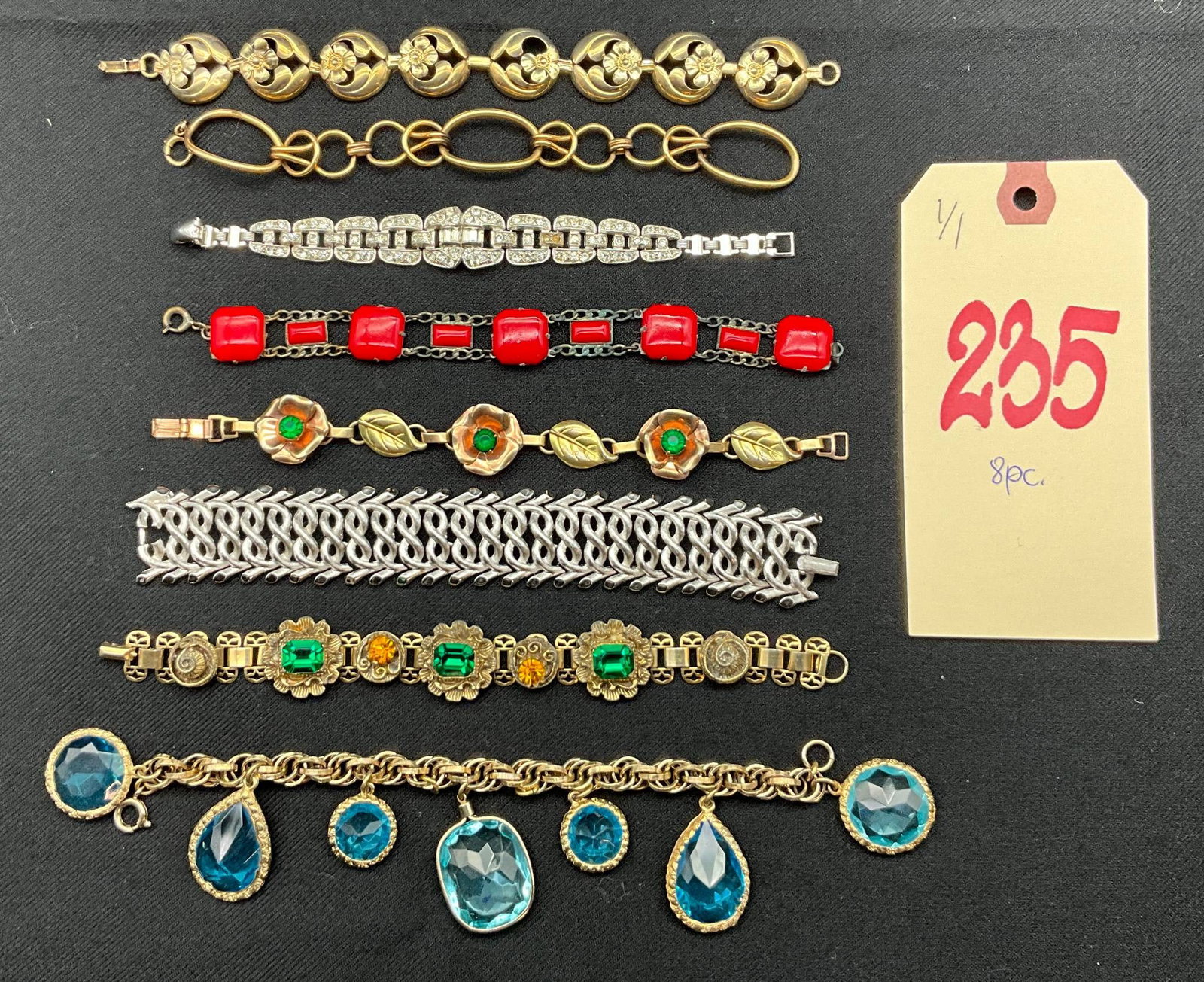 8-Piece Assorted Bracelets with Gold and Silver Tones, Includes One Marked Trifari: 8 assorted bracelets featuring gold and silver tones. Designs include floral links, chain-link styles, and accented pieces with various elements such as faux gemstones in blue, red, and green. The lot