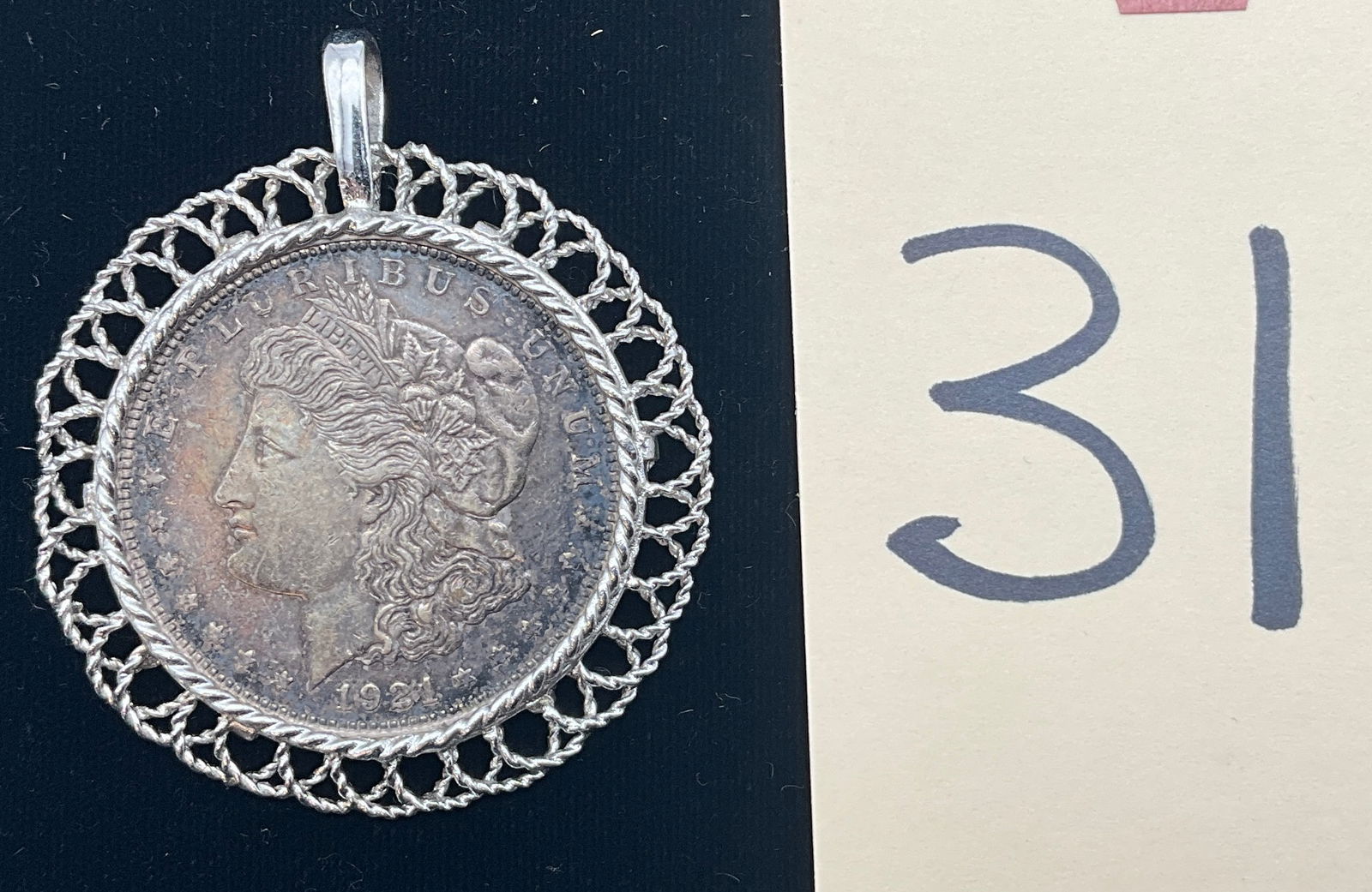 US 1921-D Morgan Silver Dollar, Silver, KM-110: KM-110. Designer: George T. Morgan. Mint mark D, Denver. Morgan obverse / Eagle reverse. The Morgan silver dollar is mounted in a sterling silver twisted-wire filigree-style pendant bezel with a bail