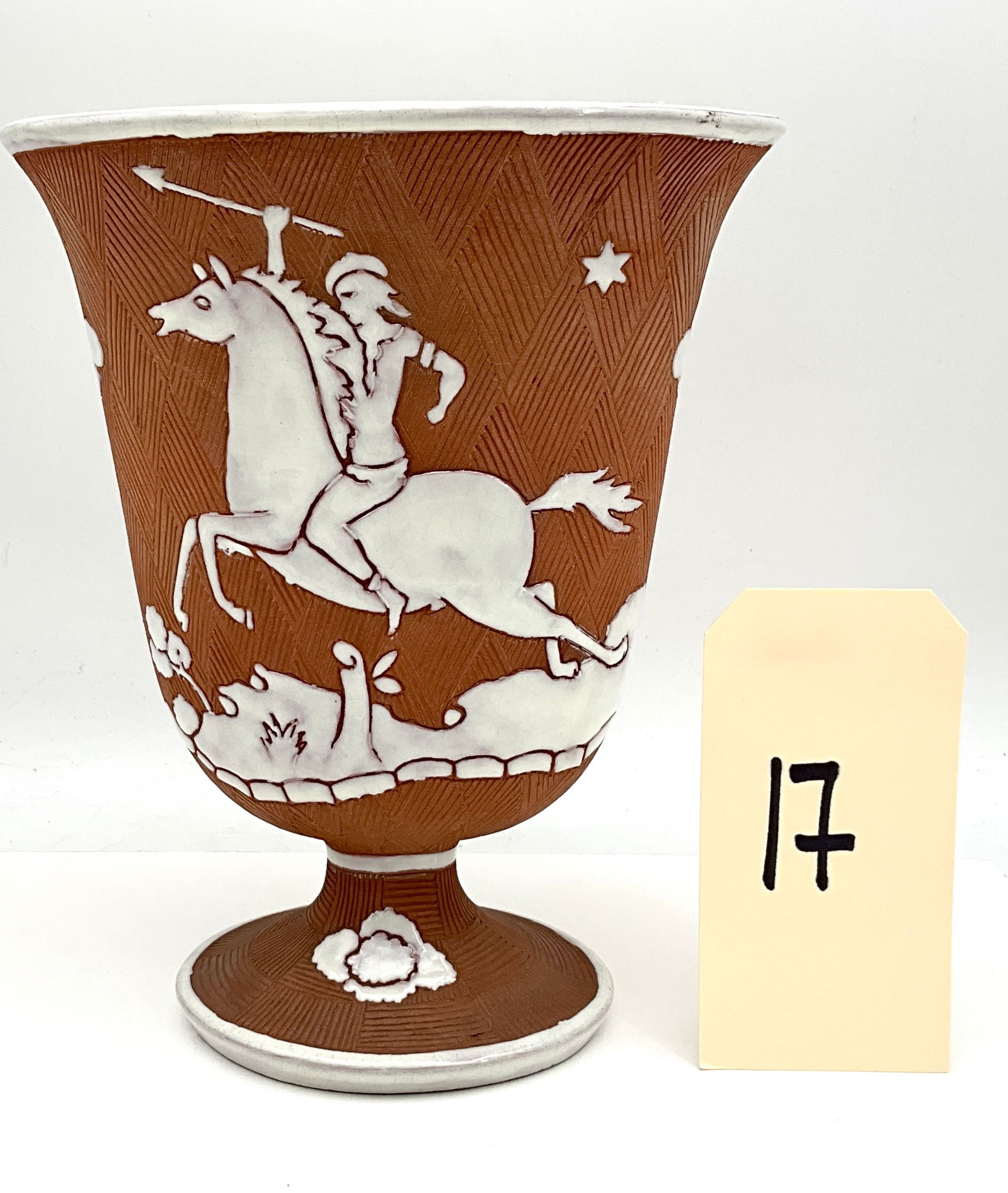 Italian Earthenware Footed Vase with Sprigged Relief Decoration: This Italian earthenware footed vase features a terracotta-colored body with an incised basketweave texture. The exterior is adorned with white glazed sprigged-style relief motifs depicting a stylized