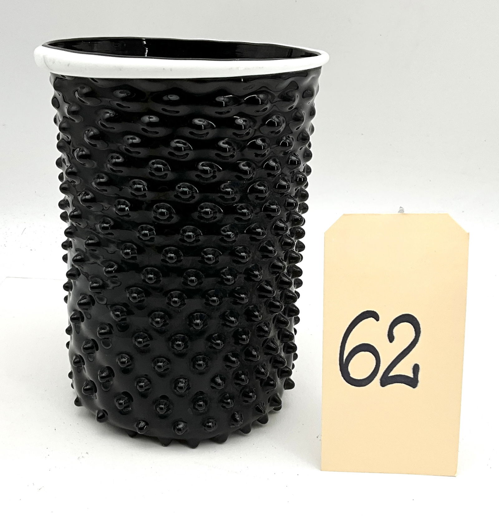 Mid-Century Modern Opaque Black Art Glass Thorn Vase with White Rim: This cylindrical art glass vase is crafted from opaque black glass featuring a prominent molded thorn or hobnail texture across the exterior. The vessel is finished with a contrasting applied white ri
