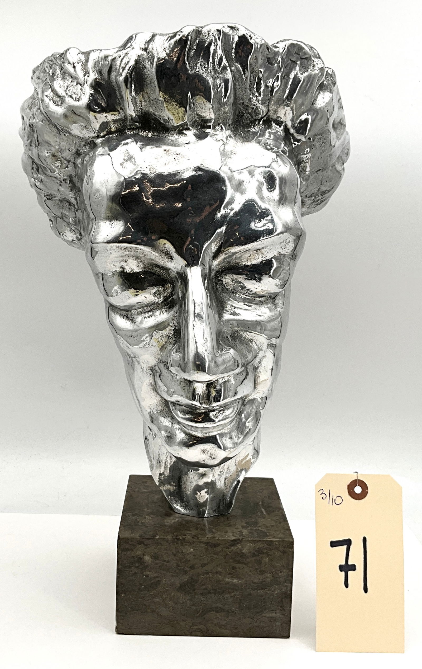 Modernist Cast Metal Mask Sculpture of a Male Face on Fossiliferous Marble Base: This modernist cast metal sculpture depicts a stylized male face with expressionist features and a swept-back, textured coiffure. The piece features a high-polish silver-toned finish on the exterior c