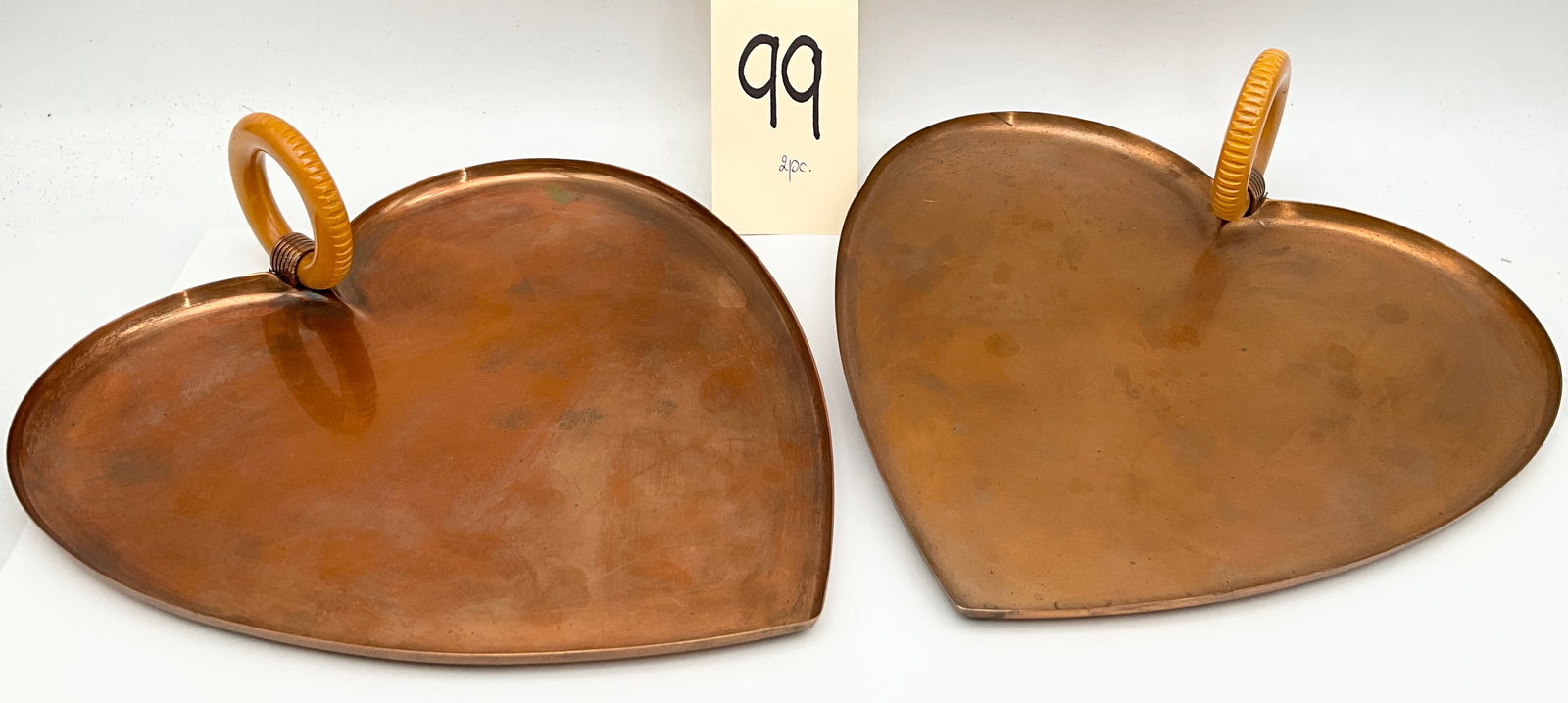 Chase USA Art Deco Copper Heart-Shaped Trays with Bakelite Handles: This pair of Art Deco heart-shaped trays was manufactured by Chase USA and features a shallow copper construction. Each tray is accented with an upright amber-colored Bakelite ring handle secured by d