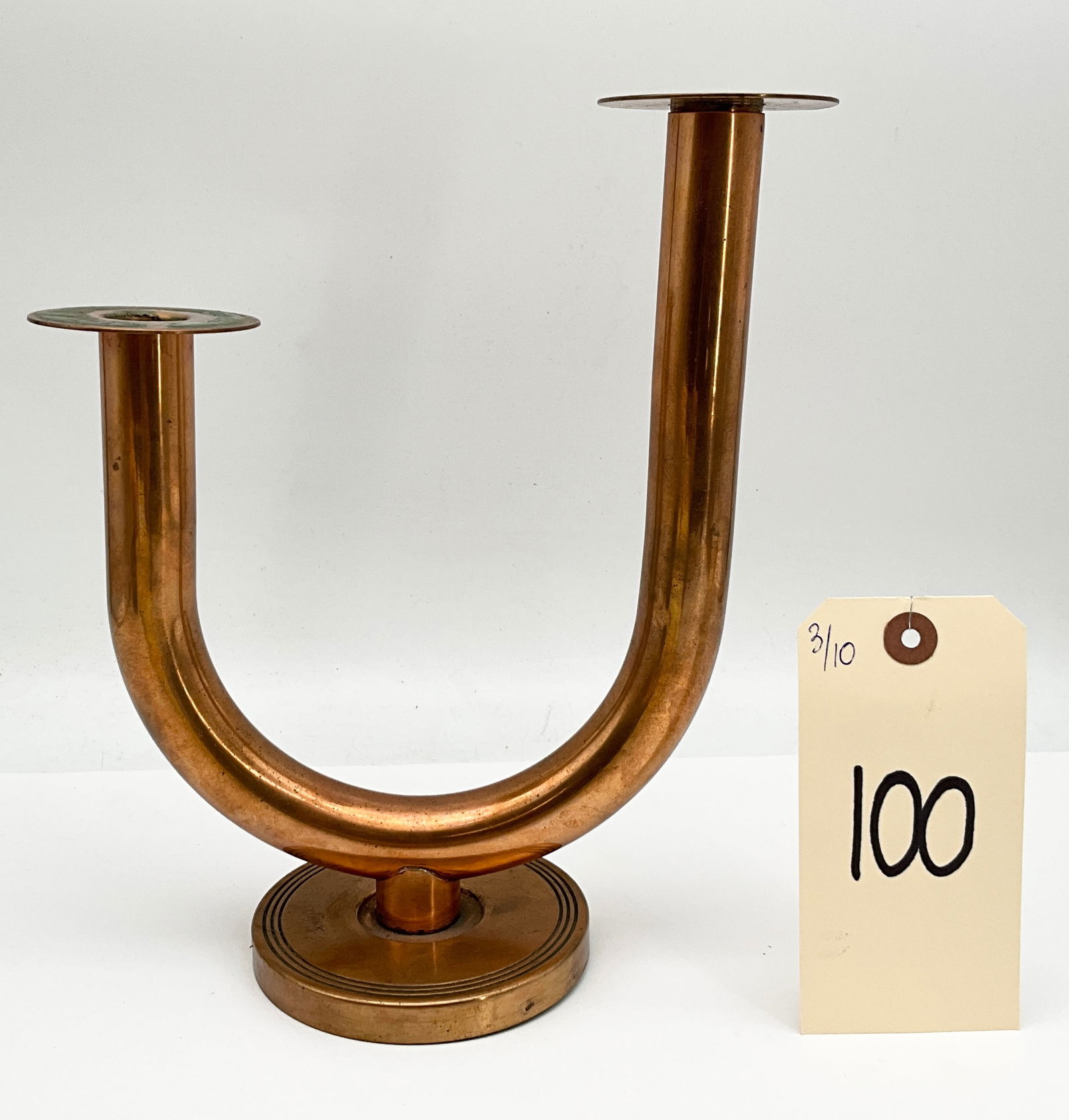 Art Deco Style Copper Double Candle Holder: This Art Deco style double candle holder likely by Coppercraft Guild is crafted from copper-toned metal with a minimalist, asymmetrical U-shaped tubular body. The two arms of varying heights each term