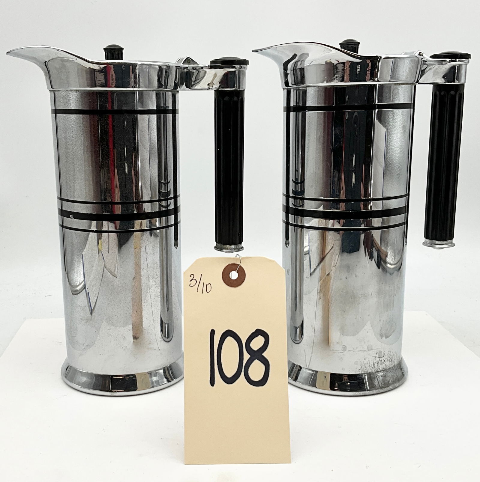 Sunbeam Art Deco Chrome-Plated Pitchers with Composite Handles: This pair of Art Deco style pitchers was manufactured by the Chicago Flexible Shaft Company under the Sunbeam brand. Each cylindrical vessel is constructed from chrome-plated metal featuring three dec