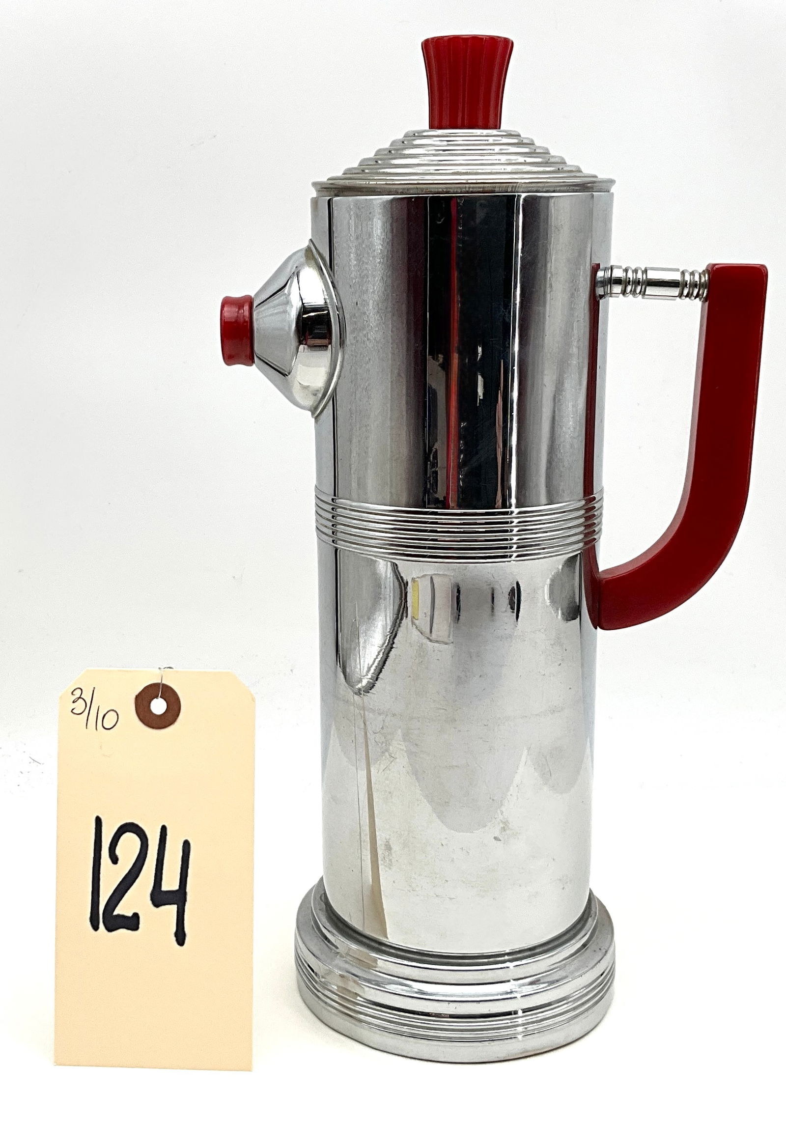 Art Deco Keystone Chrome and Red Bakelite Skyscraper Cocktail Shaker: An Art Deco Streamline Moderne cocktail shaker by Keystone, featuring a cylindrical chrome-plated body with a tiered skyscraper-style base and matching lid. The piece is accented with vibrant cherry r