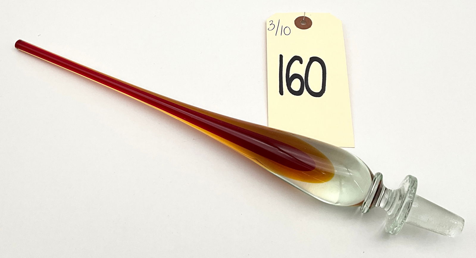 Art Glass Decanter Stopper, Red and Amber: This 13-inch art glass stopper features an elongated teardrop form crafted using the sommerso technique with a deep red core encased in amber and clear glass. The piece is designed with a clear glass