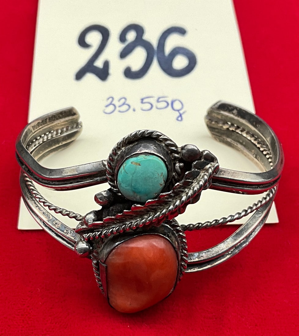 Sterling Silver Navajo Cuff Bracelet with Turquoise and Coral: This vintage Navajo cuff bracelet is crafted in sterling silver and features a large, irregularly shaped orange-red cabochon that appears to be coral alongside a smaller blue-green cabochon that appea