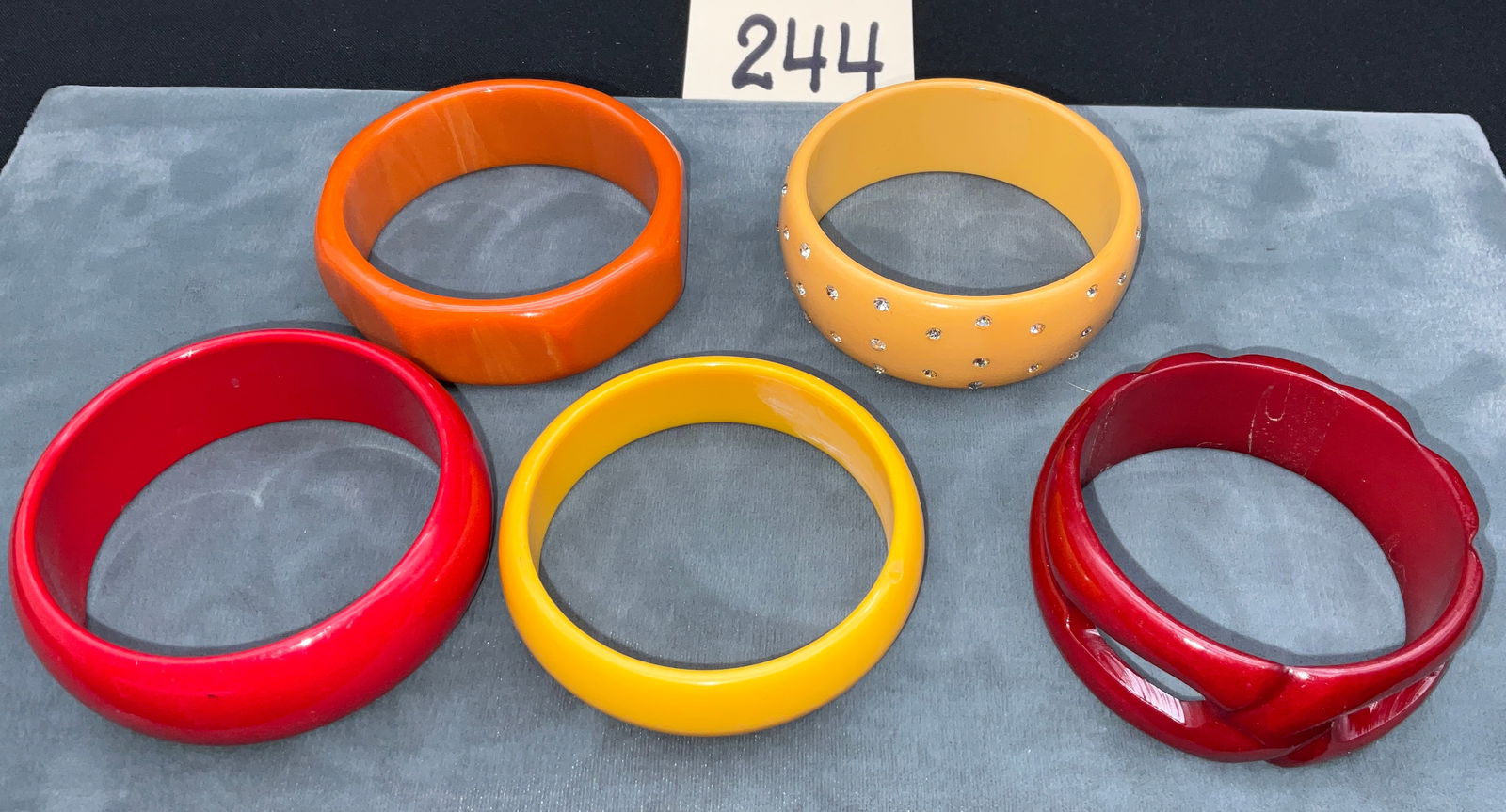 Resin Bangle Bracelet Collection with Rhinestone and Carved Accents: This collection features five vintage-style resin slip-on bangles in a warm autumnal palette of red, orange, and yellow. The set includes a faceted orange piece, a butterscotch-toned bangle inset with