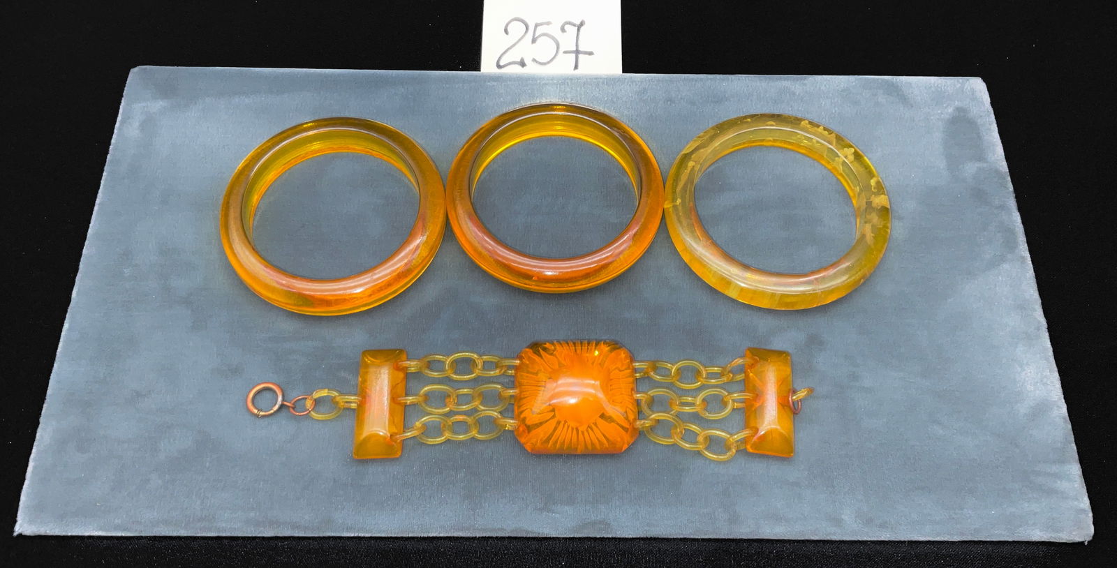 Copper-toned and Carved Apple Juice and Butterscotch Bakelite Bracelet Collection: This collection features three Bakelite bangles and one triple-strand link bracelet in translucent apple juice and butterscotch tones. The link bracelet showcases a central panel with an intaglio