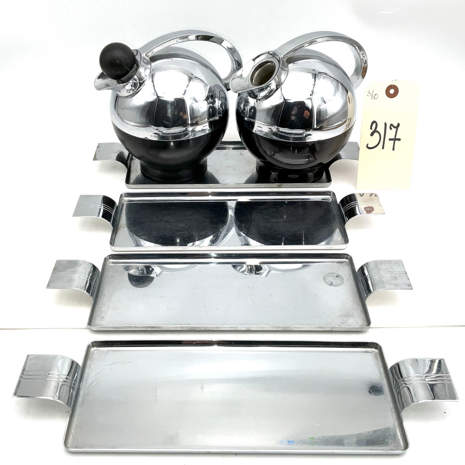 Raymond Loewy for American Thermos Co. Art Deco Spherical Miracle Carafes and Revere Trays, circa: This set features a pair of Spherical Miracle vacuum carafes designed by Raymond Loewy for The American Thermos Bottle Co., showcasing a classic Art Deco chrome and black Bakelite aesthetic. Accompany