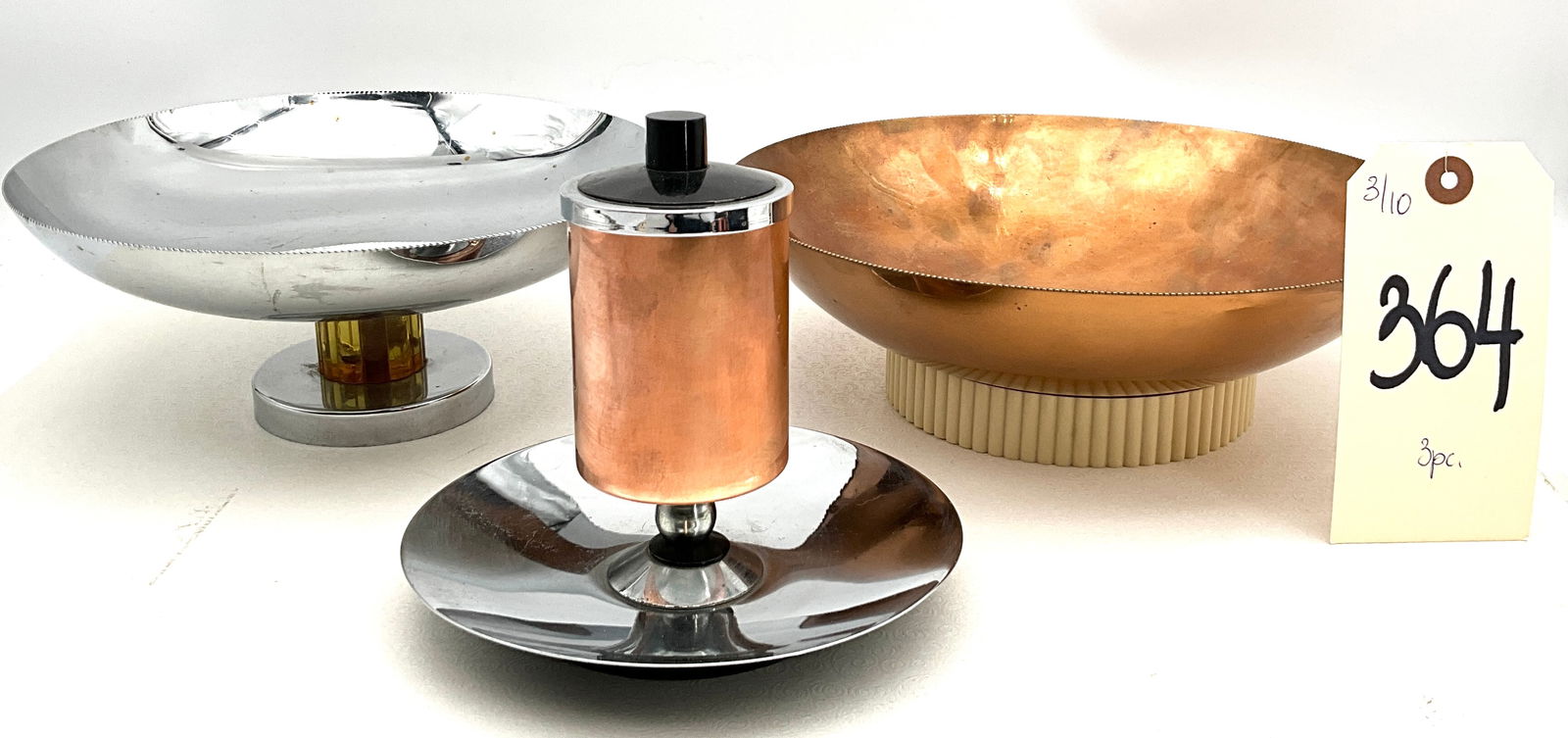 Three American Art Deco Metalware Pieces, Farberware and Chase: This collection includes a Farberware chrome-plated pedestal bowl with a faceted amber-colored stem and a Chase copper pedestal bowl featuring a cream-colored ribbed plastic base. Completing the lot i