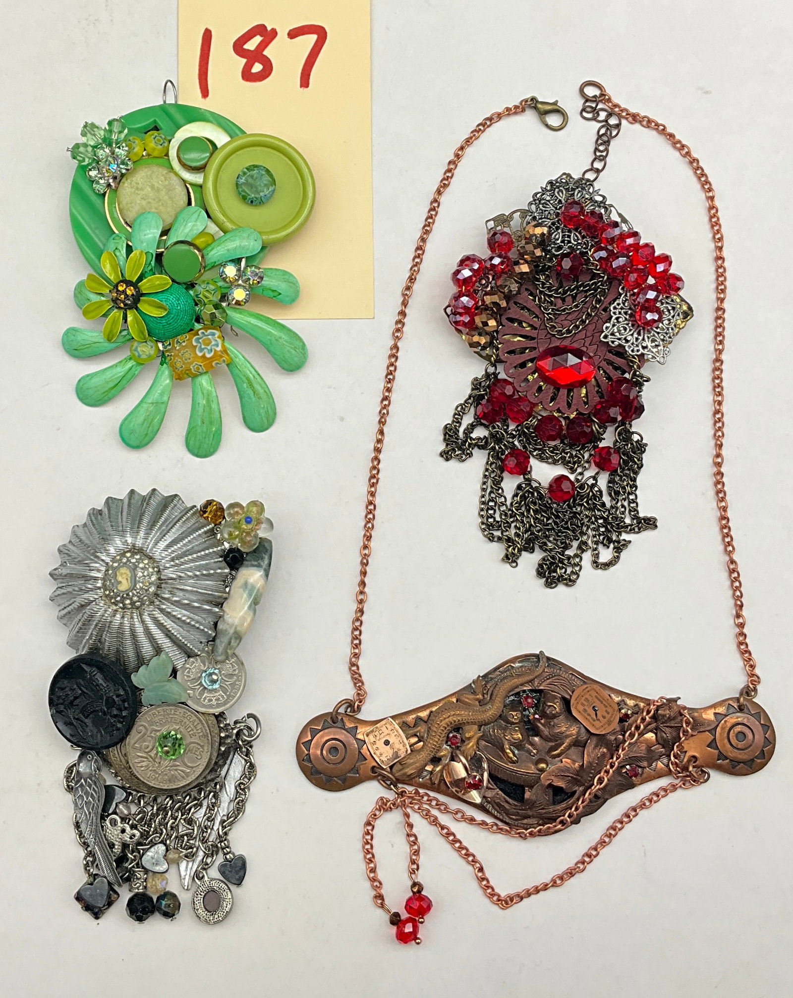 A Collection of Four Sarah Jane Signed Mixed Media Assemblage Art Jewelry Pieces: This collection of contemporary mixed-media jewelry features three oversized brooches and one narrative necklace, each hand-signed by the artist Sarah Jane on a black textured backing. The pieces are