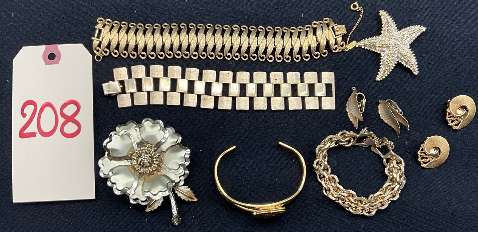 An Assortment of Vintage Signed Goldtone Costume Jewelry: This collection features gold-tone base metal pieces including a Monet textured scroll link bracelet and a Sarah Coventry geometric panel bracelet with a linen finish. The group includes two pairs of