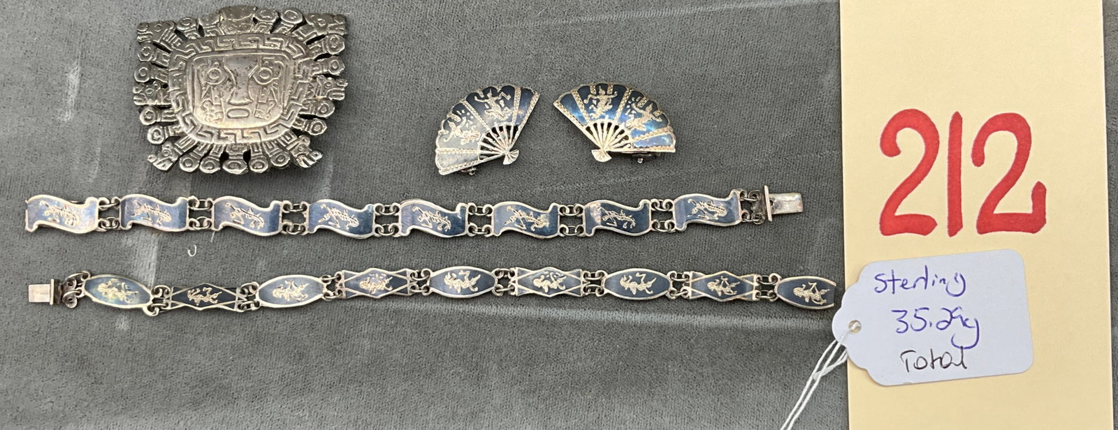 A Collection of Sterling and .900 Silver Jewelry: This collection of silver jewelry features a Reyes Plata 900 brooch and various Siam niello enamel pieces. The brooch displays a stylized Pre-Columbian face with geometric borders and carries the