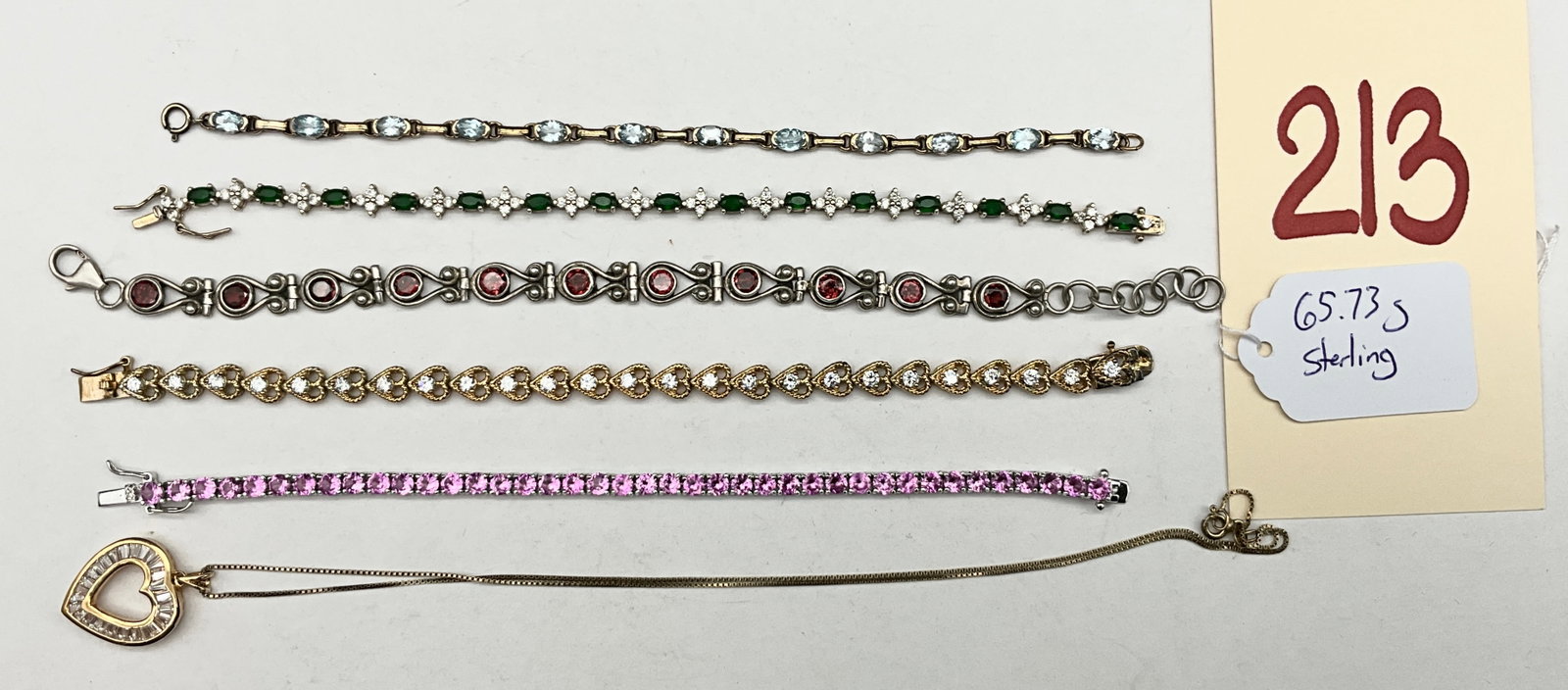 A Collection of Sterling Silver and Colored Gemstone Jewelry: An assortment of sterling silver jewelry includes five bracelets and one heart-shaped pendant on a box chain. The set features a pink gemstone tennis bracelet, a green and clear stone line bracelet,