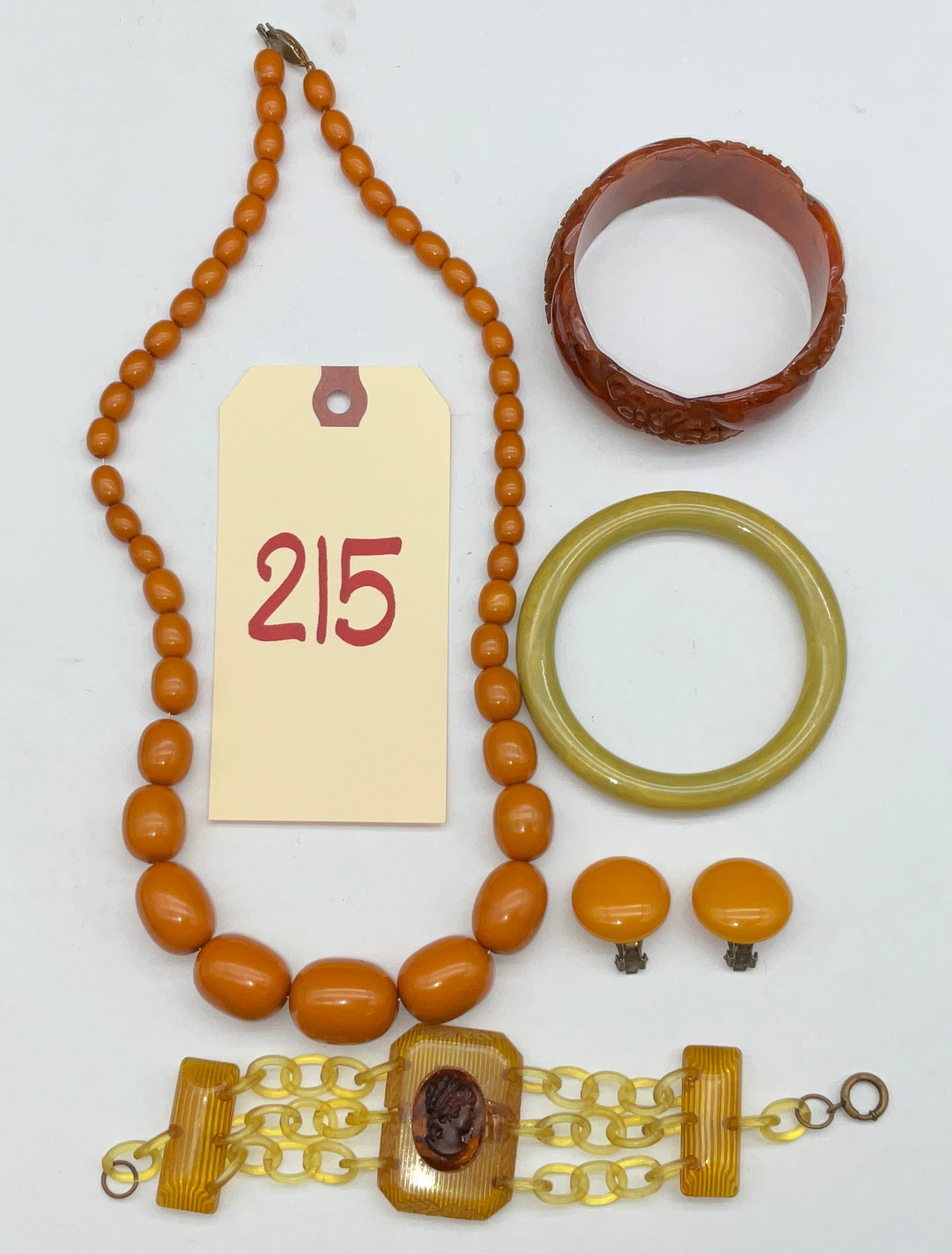 A Collection of Vintage Bakelite and Early Plastic Costume Jewelry: This collection of vintage jewelry features butterscotch, chartreuse, and dark amber-toned Bakelite and early plastic components. The assembly includes a graduated necklace of polished butterscotch ov