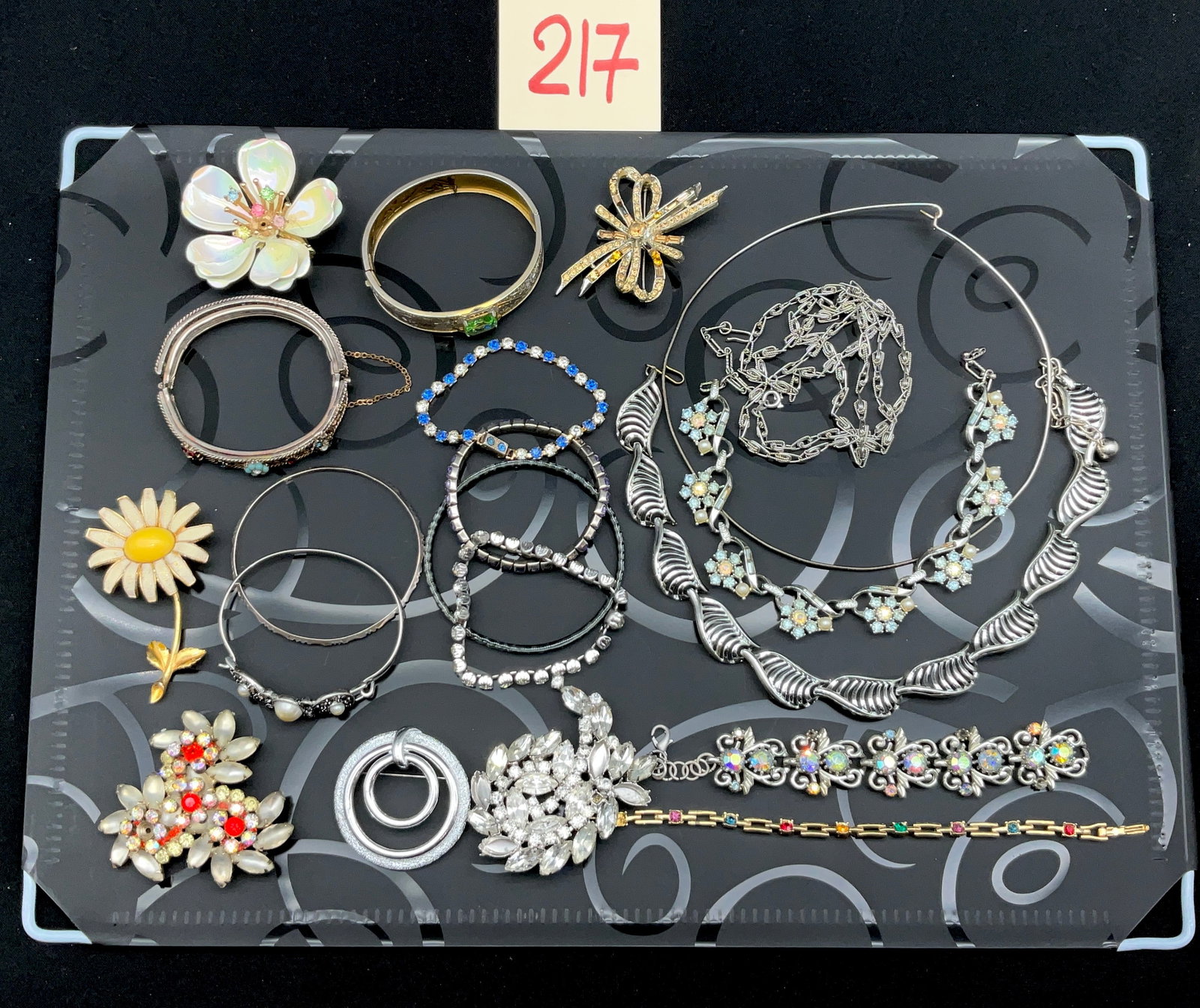 A Collection of Vintage Mid-Century Costume Jewelry: This collection of mid-century costume jewelry features an assortment of necklaces, bracelets, and brooches in silver-tone and gold-tone metals. Signed pieces include a Kramer of New York clear rhines