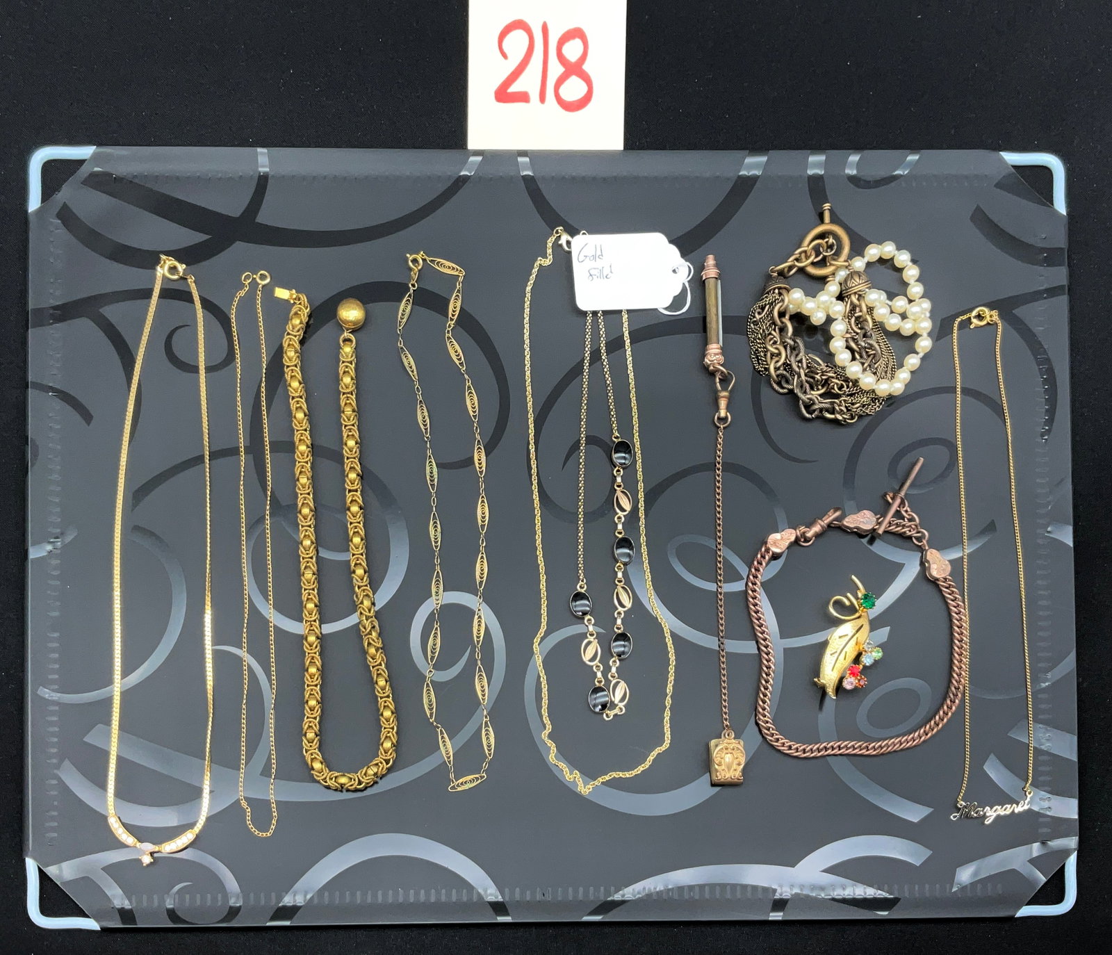 A Collection of Vintage Gold-Filled and Costume Jewelry: This assortment includes yellow-toned necklaces in byzantine, herringbone, and filigree styles alongside a black cabochon station chain. The lot features a multi-strand faux pearl bracelet, a