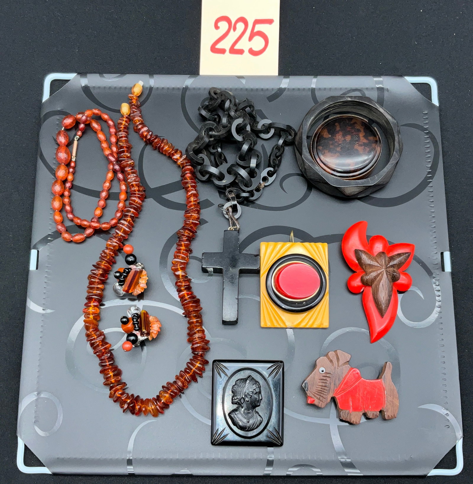 A Collection of Vintage Bakelite, Amber, and Costume Jewelry: This assortment of vintage costume jewelry includes Bakelite, amber, and carved wood components in Art Deco styles. A highlight is the square pendant signed Sarah Jessen, featuring a red cabochon and