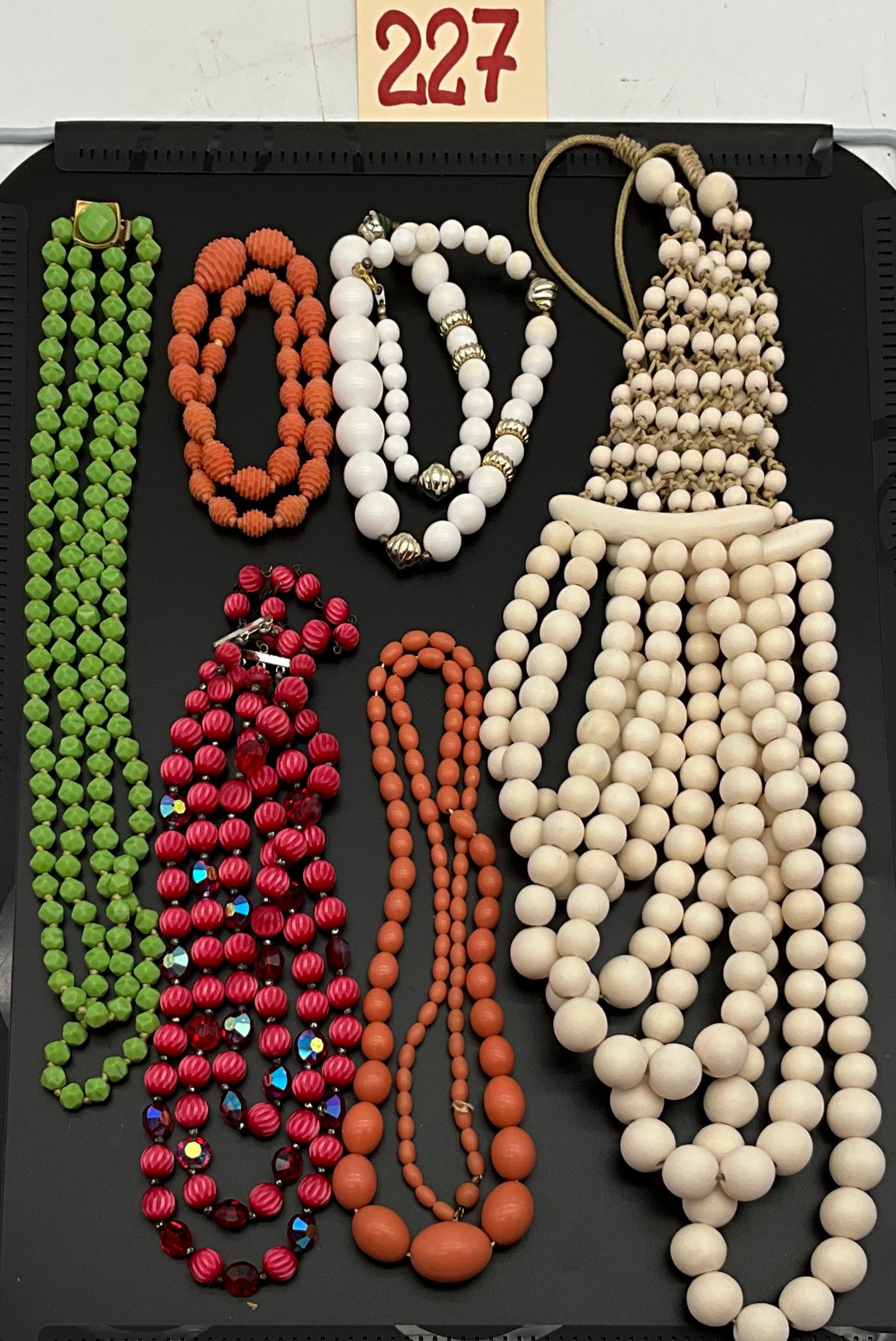 An Assortment of Vintage Multi-Strand Plastic Beaded Costume Jewelry Necklaces: This group of vintage costume jewelry features multiple multi-strand necklaces in a vibrant palette including avocado green, ruby red, pumpkin orange, and cream. The collection includes a triple-stran