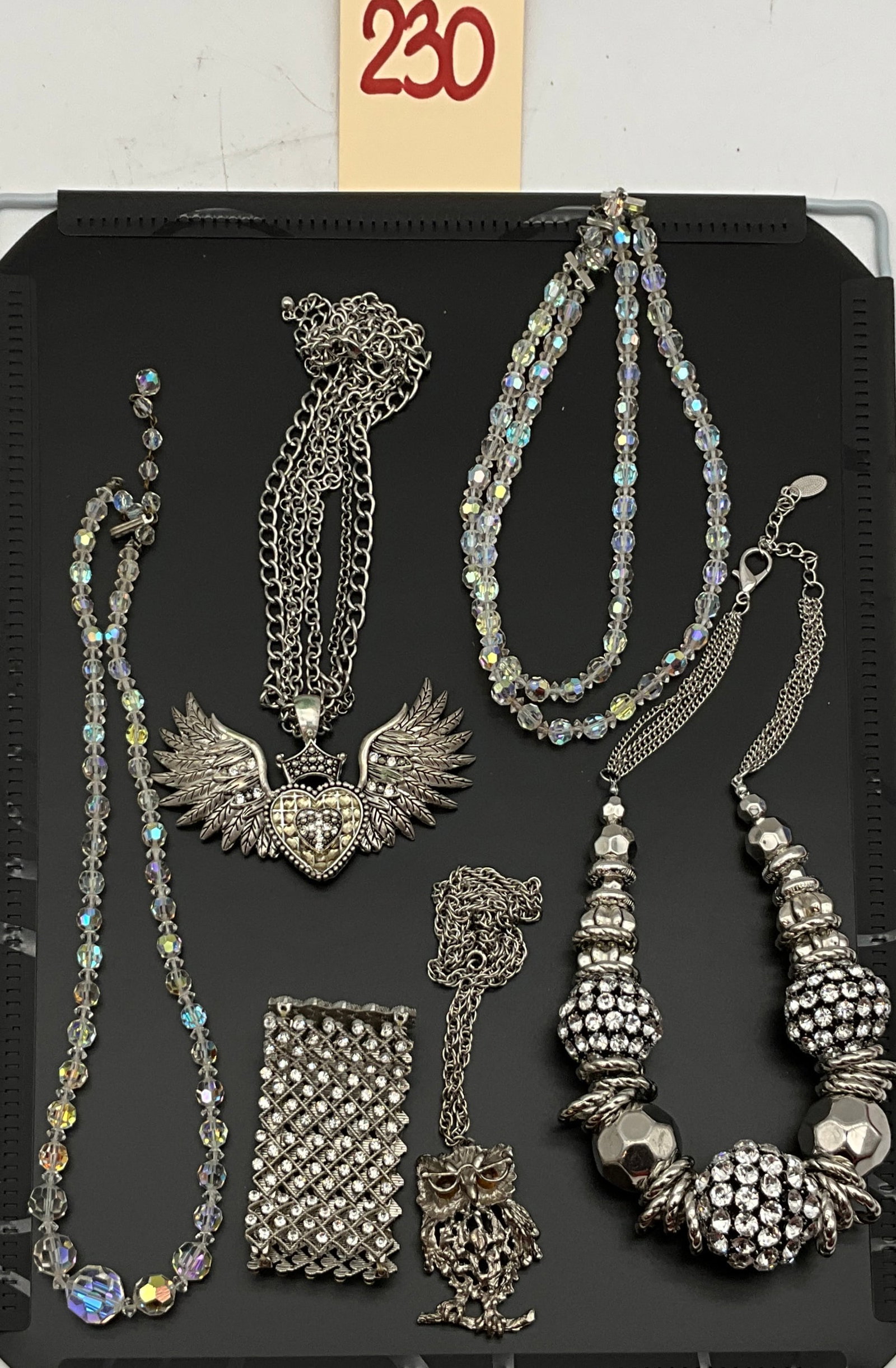 Six Pieces of Silver-Tone Rhinestone and Iridescent Glass Costume Jewelry: This lot comprises six pieces of silver-tone costume jewelry including five necklaces and one rhinestone mesh bracelet. The selection features a large crowned winged heart pendant with clear