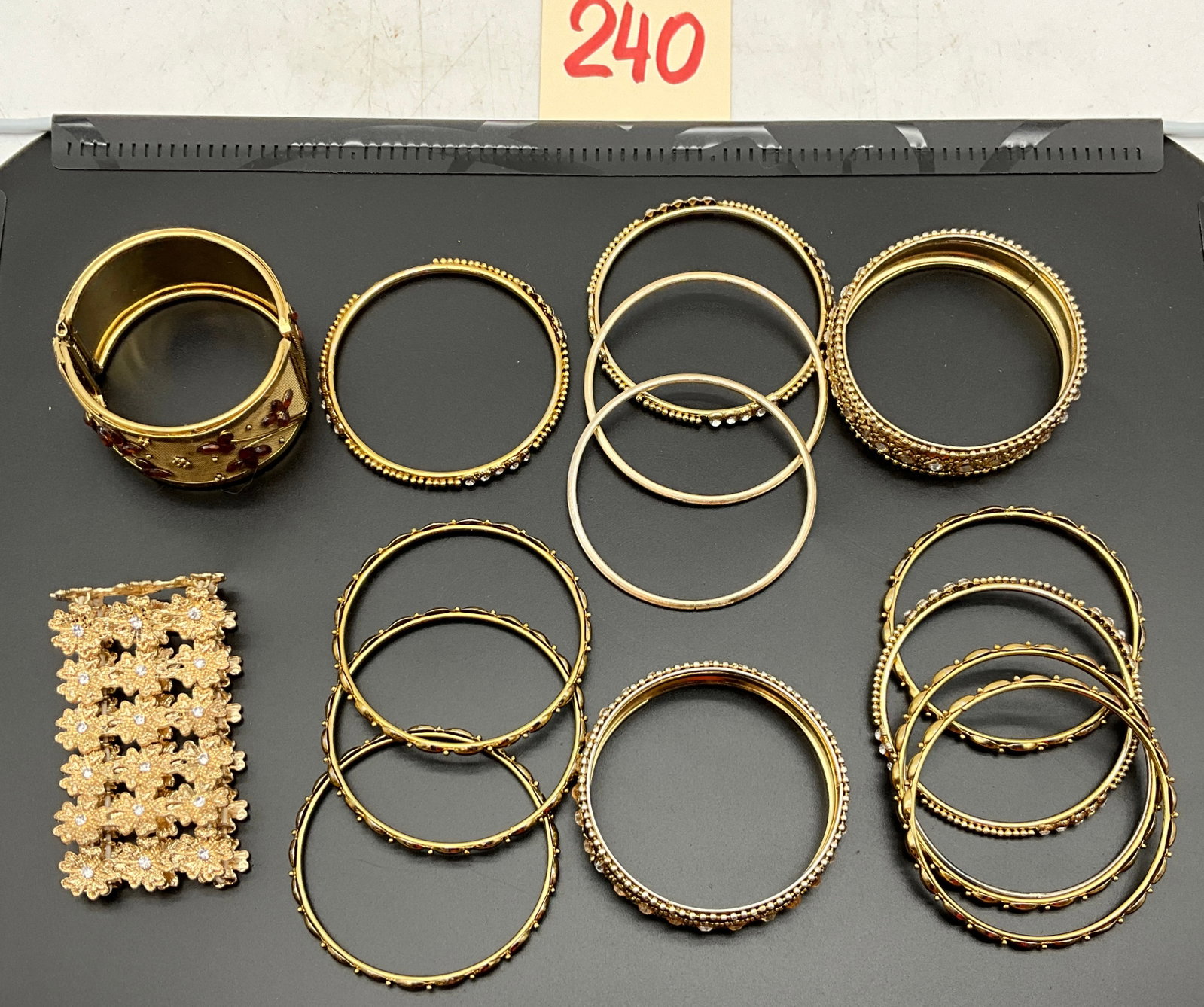 Assortment of Gold Tone Costume Jewelry Bracelets and Bangles: This collection includes assorted gold-tone costume jewelry bracelets and bangles in various widths and styles. Featured pieces include a wide hinged mesh cuff bracelet with applied amber-colored ston