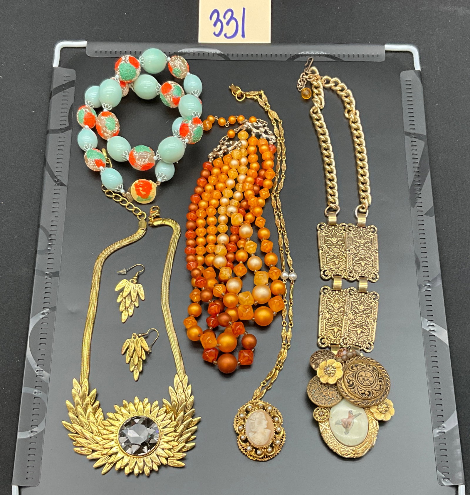 An Assortment of Vintage and Contemporary Costume Jewelry: This collection of costume jewelry features an assortment of necklaces, matching drop earrings, and a brooch fabricated from gold-tone metal, shell, glass, and plastic. Notable pieces include a large 