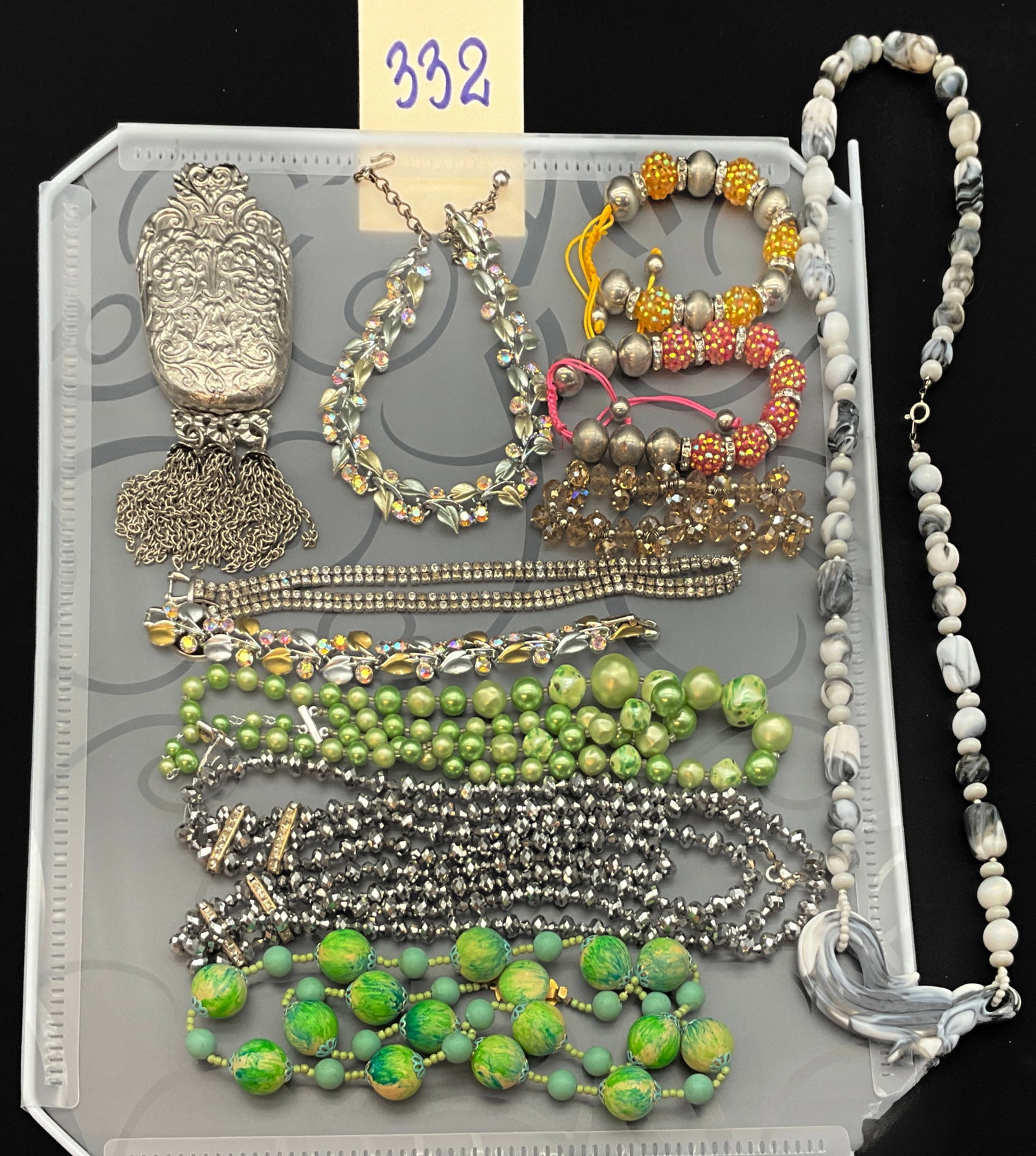 A Collection of Vintage Costume Jewelry: This collection features approximately 10 pieces of vintage costume jewelry including a designer clip and various necklaces and bracelets. The silver-tone tassel clip bears a circular embossed mark