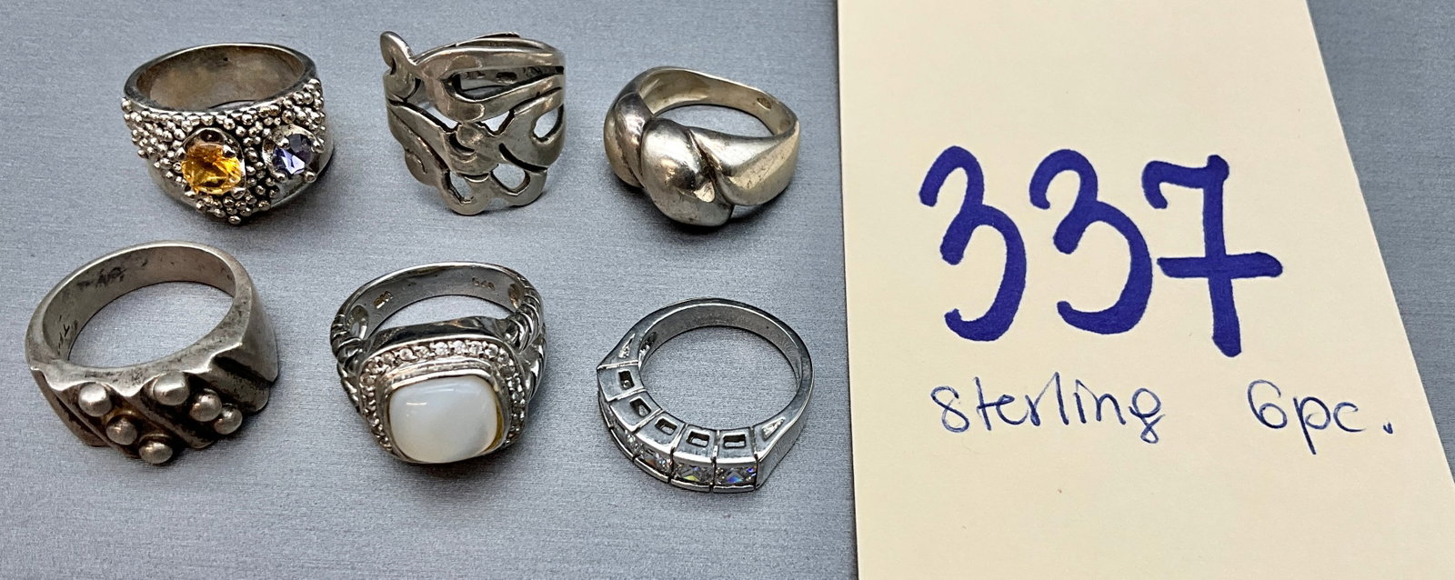 A Collection of Vintage Sterling Silver Rings with Gemstones: This lot features six contemporary silver rings, including a wide granulated band set with yellow and purple stones and a cushion-cut mother-of-pearl ring with clear stone accents. Other styles