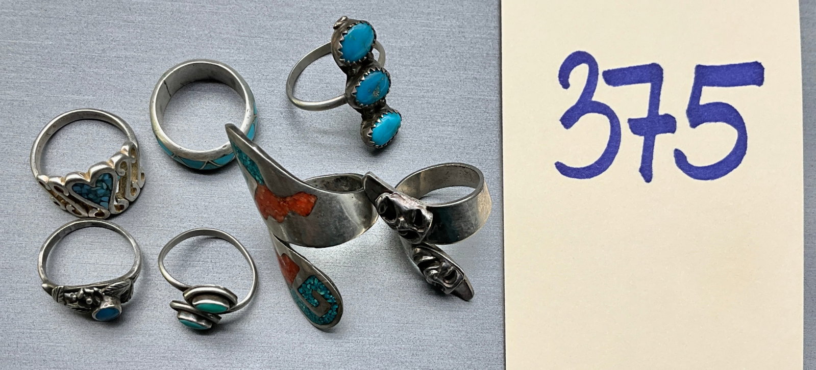 A Collection of Seven Vintage Southwestern Style Silver and Turquoise Rings: This collection of seven rings features assorted band, bypass, and wide wrap-around designs fabricated from silver and silver-toned metal. The pieces are accented with turquoise cabochons and chip-inl