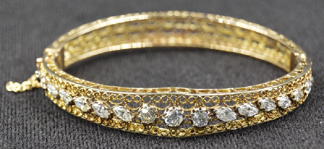 14k Yellow Gold and Diamond Bangle Bracelet: An openwork scrolling setting having 17-diamonds consisting of a central .4 carat round diamond, flanked on either side by a .32 carat round diamond, each flanked by 5-graduated marquise diamonds grad
