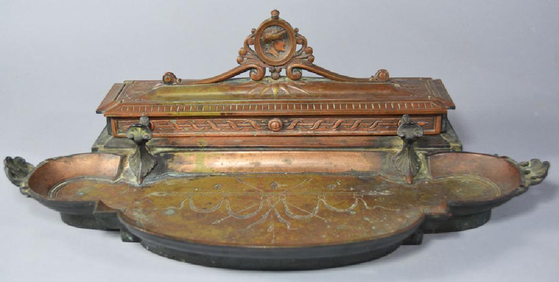 19th C. Bronze Inkwell Stand: having a central medallion on inkwell cover, opening to reveal four glass inkwells being raised behind a pen holder and tray, Neoclassical motifs throughout, 16" long, 10" deep, 5 1/2" high.