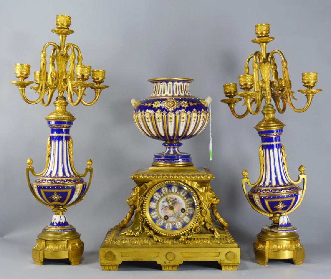 French Bronze Ormolu and Porcelain Garniture Set: Comprising a mantle clock with hand painted porcelain and enameled face and urn, having Lion and wreath handles, 15" high, and a pair of candelabras, each being approx. 20" high