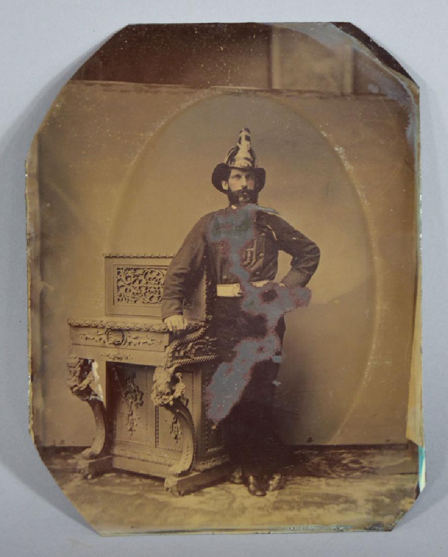 Full-Plate Tintype of a Fireman: Bearded fireman wearing a fireman's helmet with an emblem from Manchester, NH and standing next to a highly carved piano, 6 1/2" x 8 3/8"