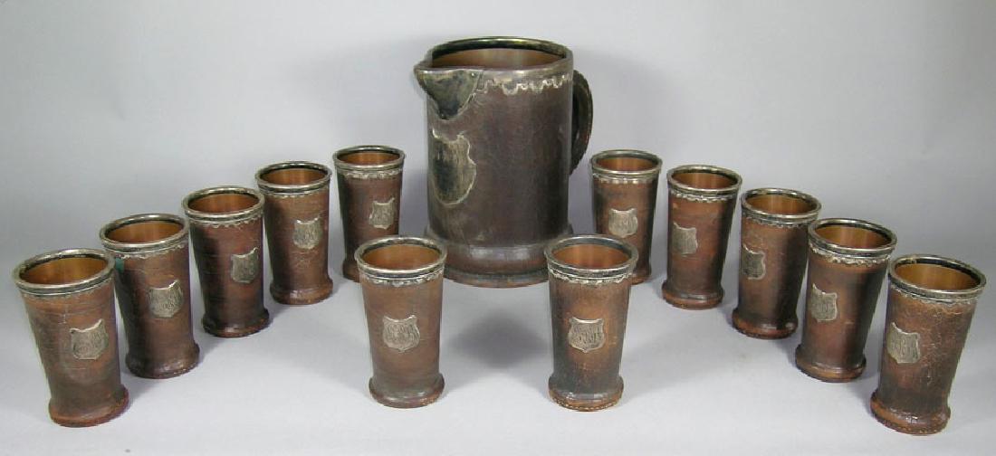A Very Rare San Francisco Earthquake Gorham: the pitcher being of circular form with a flaring base, leather with copper lining and having a Gorham sterling silver decorative rim, spout and shield form cartouche, the cartouche bearing the scroll