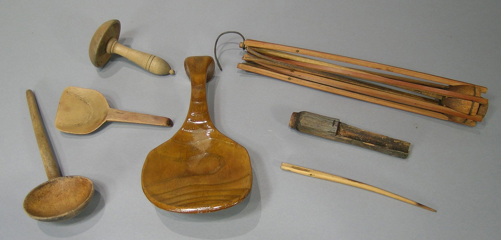Seven Antique Treen Items: comprising a carved ladle, a small carved scoop, a carved round ladle, a maple sugar tap, a sewing accessory (possibly Shaker), a wooden needle and a swift.