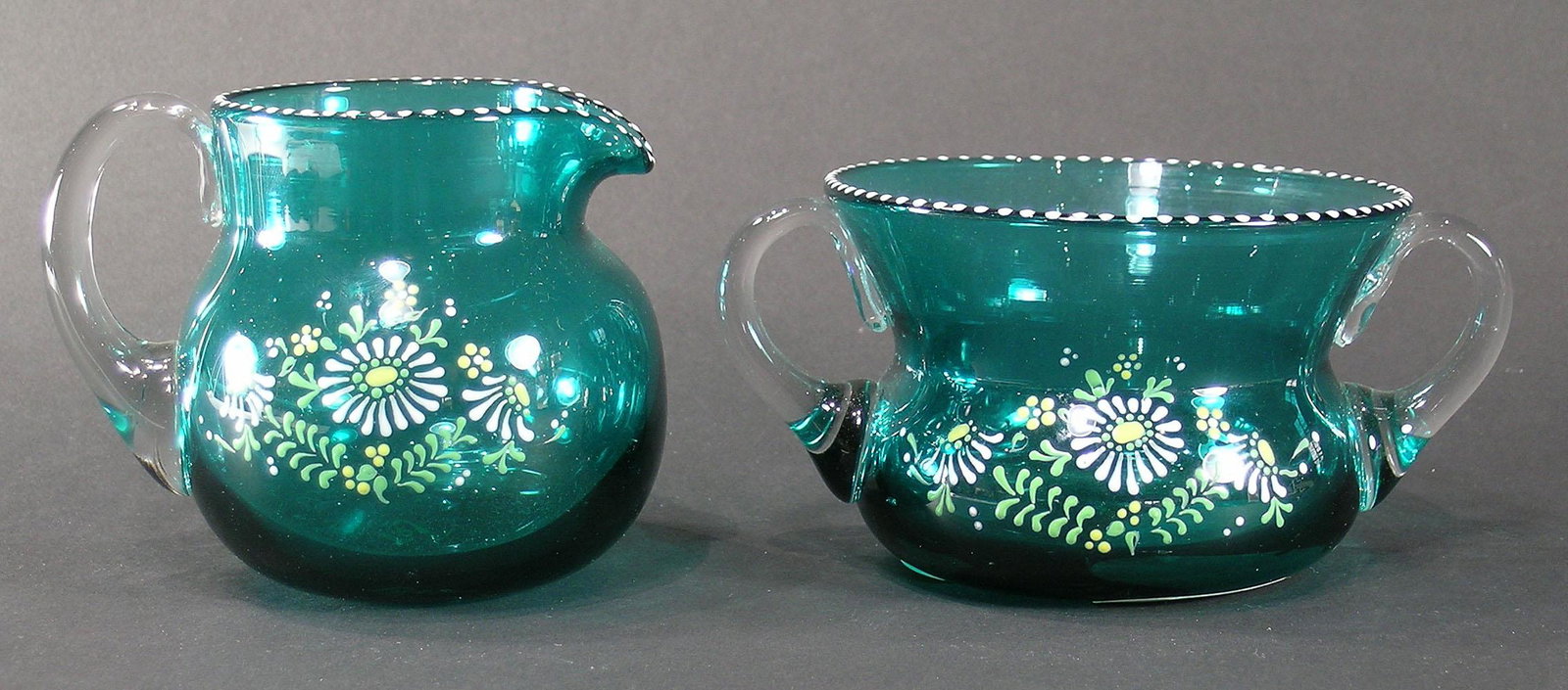 PAIRPOINT ENAMELED GLASS SUGAR BOWL AND CREAMER: aqua blue with clear glass handles, having enamel floral decoration and beaded rims, both signed with an enameled Pairpoint mark on the underside, sugar bowl 2 3/4" high, creamer 3 1/2" high. NOTE: Th