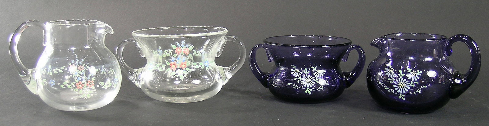 TWO SETS OF BRYDEN PAIRPOINT ENAMELED GLASS SUGAR BOWLS: one amethyst glass, one crystal both signed by Cynthia Bryden, amethyst sugar bowl 2 5/8" high, amethyst creamer 3" high, crystal sugar bowl 3" high, crystal creamer 3 1/2" high