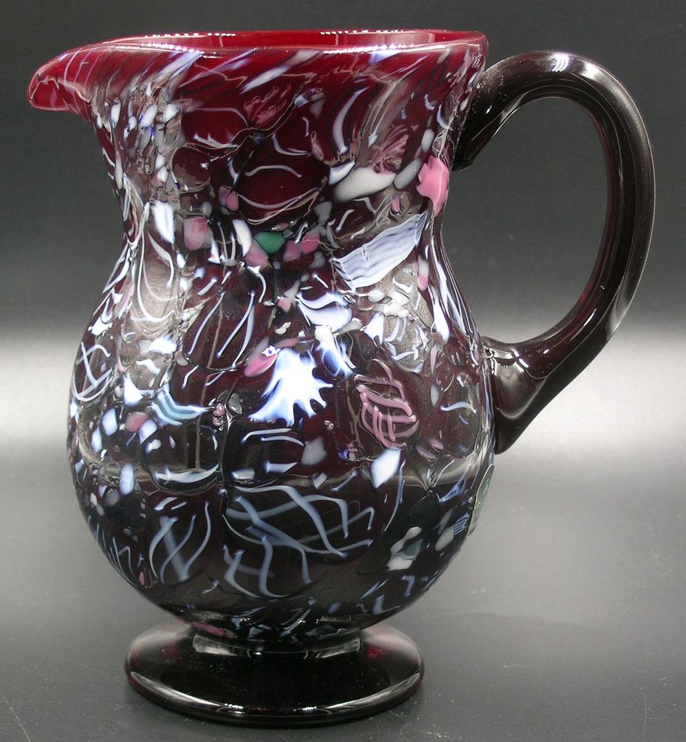 BRYDEN PAIRPOINT GLASS ENAMELWARE PITCHER: deep ruby with polychrome cane and frit rolled-on decoration, 4" dia. body, 6 1/4" high. Note: Former Allen Collection