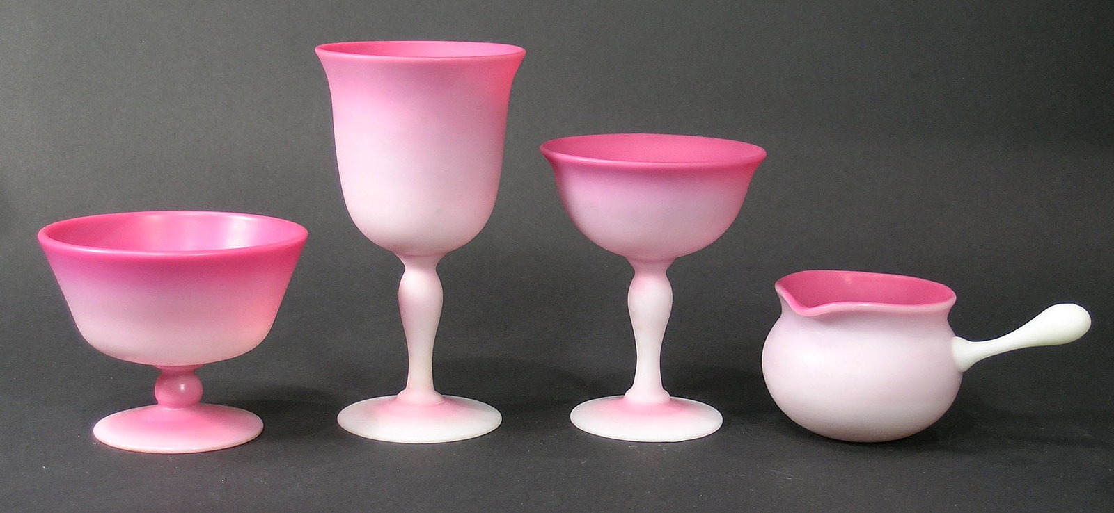 FOUR PAIRPOINT PEACHBLOW GLASS TABLE ARTICLES: all having matte finish, comprising a champagne glass, 5" high, a sherbet dish, 3 1/2" high, a handled cream soup cup, 2 5/8" high, and a wine glass, 6 1/2" high, all having polished pontils