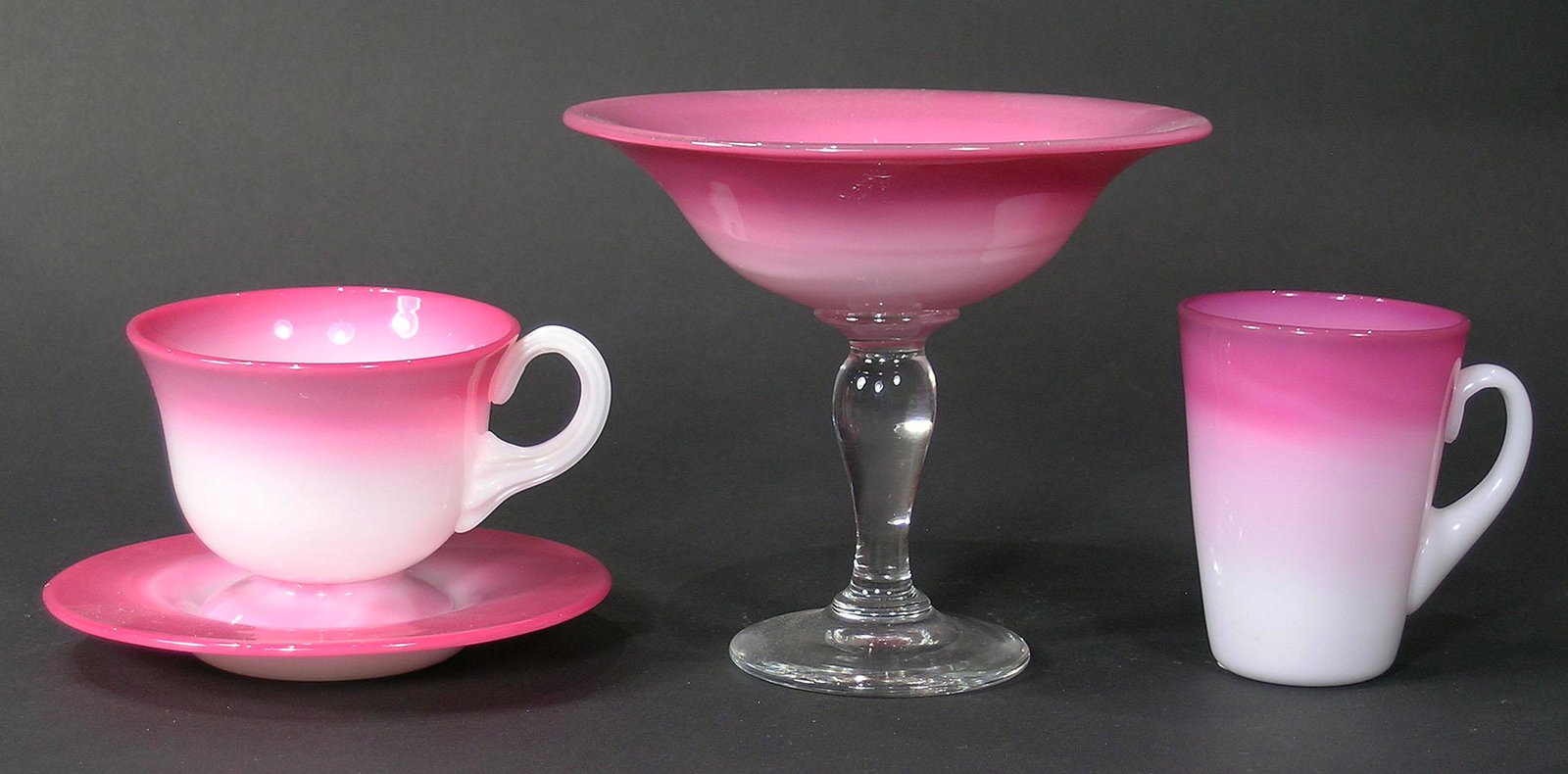 FOUR PAIRPOINT PEACHBLOW GLASS TABLE ARTICLES: all having gloss finish, comprising a comport with clear glass stem and base, 6" dia., 5" high, a tea cup and saucer, and handled cup. The comport is from the Duff and Molly Allen Collection