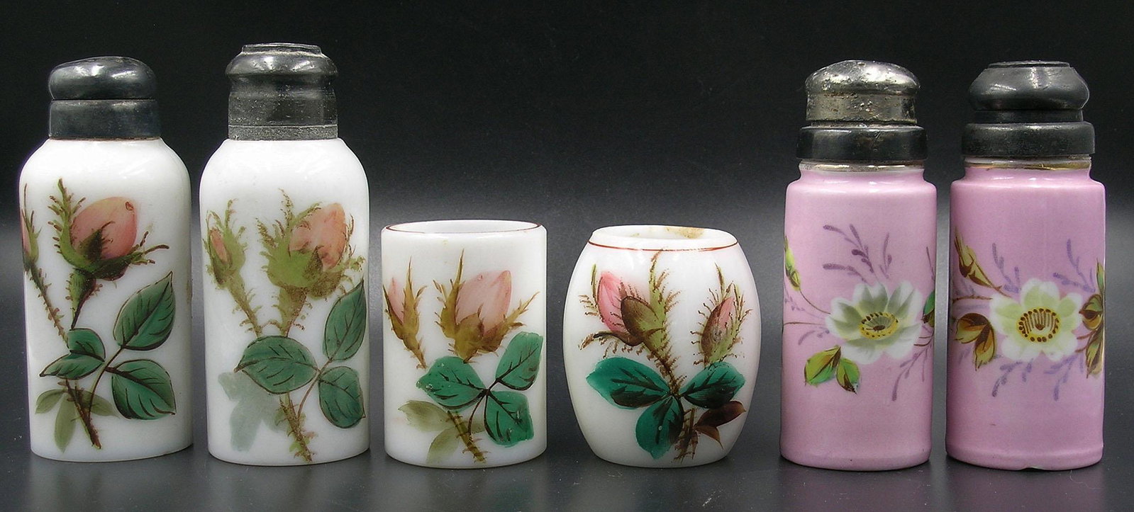 SIX ANTIQUE MILK GLASS TABLE ARTICLES: all having hand painted floral and leaf decoration, comprising a four piece set with roses, being a salt and pepper shaker and two toothpick holders, and two-painted pink shakers, the tallest being 4 