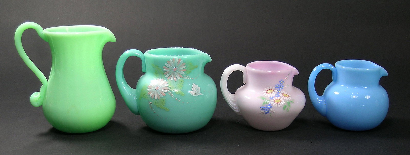 EIGHT PAIRPOINT GLASS CREAMERS: all opaque glass, various colors and shapes,, two being peachblow, five having hand painted enamel floral and leaf decoration, various sizes with the largest being 4 1/4" high.