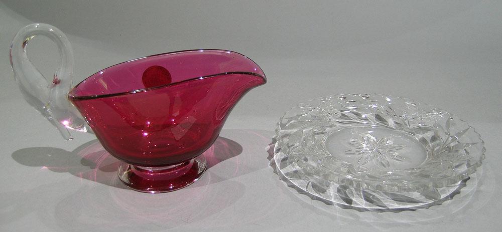 GUNDERSEN PAIRPOINT GRAVY BOAT WITH SWAN HANDLE: Cranberry glass body having a colorless glass swan handle and base, round silver label, 4 1/2" high to top of handle; on a Pairpoint underplate with cut Colias pattern decoration, 6" dia.