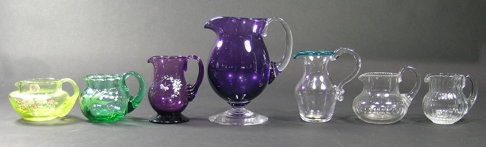 SEVEN PAIRPOINT GLASS CREAMERS: various colors and shapes, three having hand painted enamel floral and leaf decoration, one cut glass, the largest being 5 3/4" high