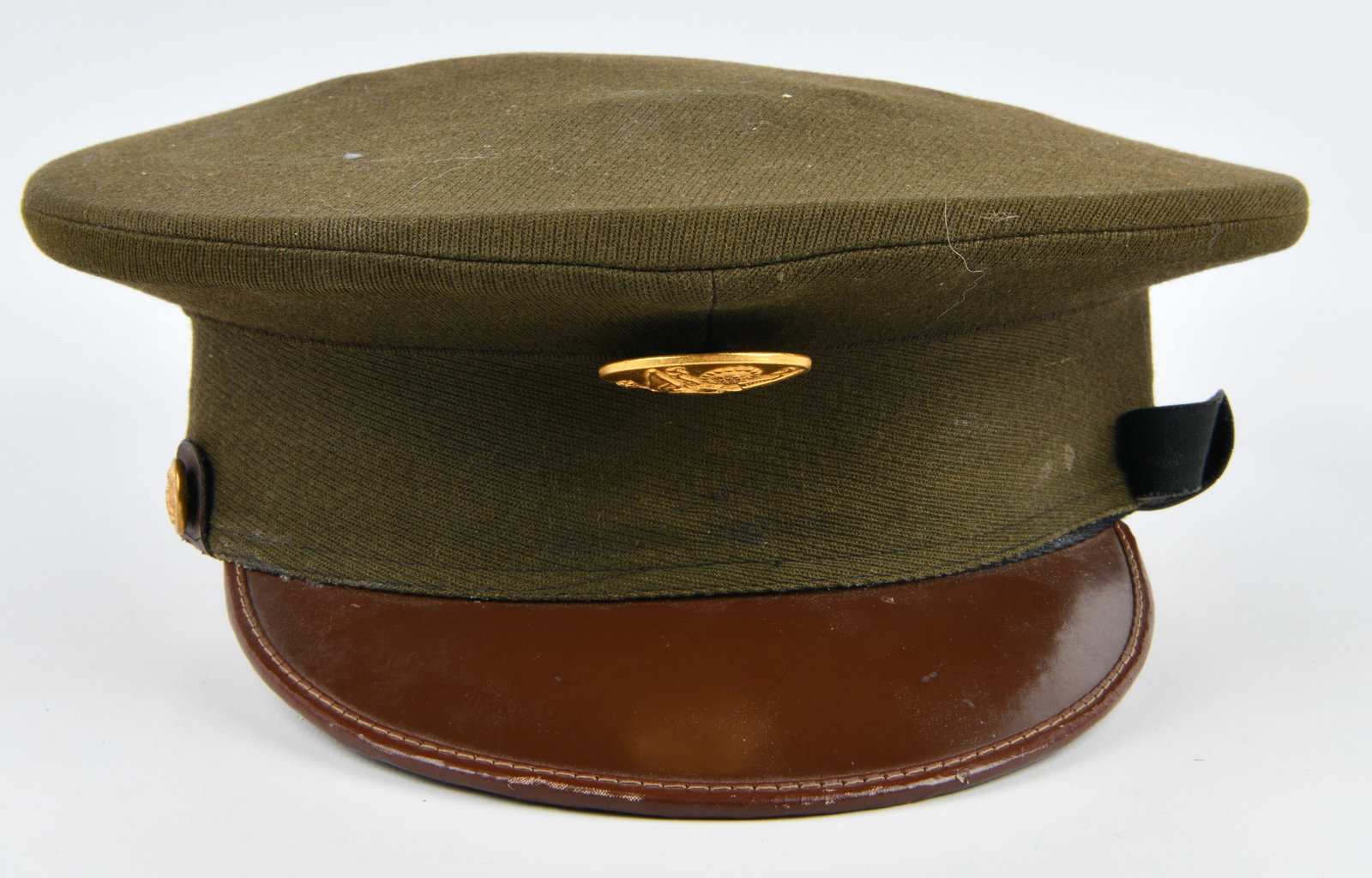 WWII US Army Enlisted Visor Cap by Imperial: A WWII US Army Enlisted Visor Cap, olive drab in color and constructed from a wool or wool blend fabric. The cap features a prominent brass-toned insignia on the front depicting the Great Seal of the 