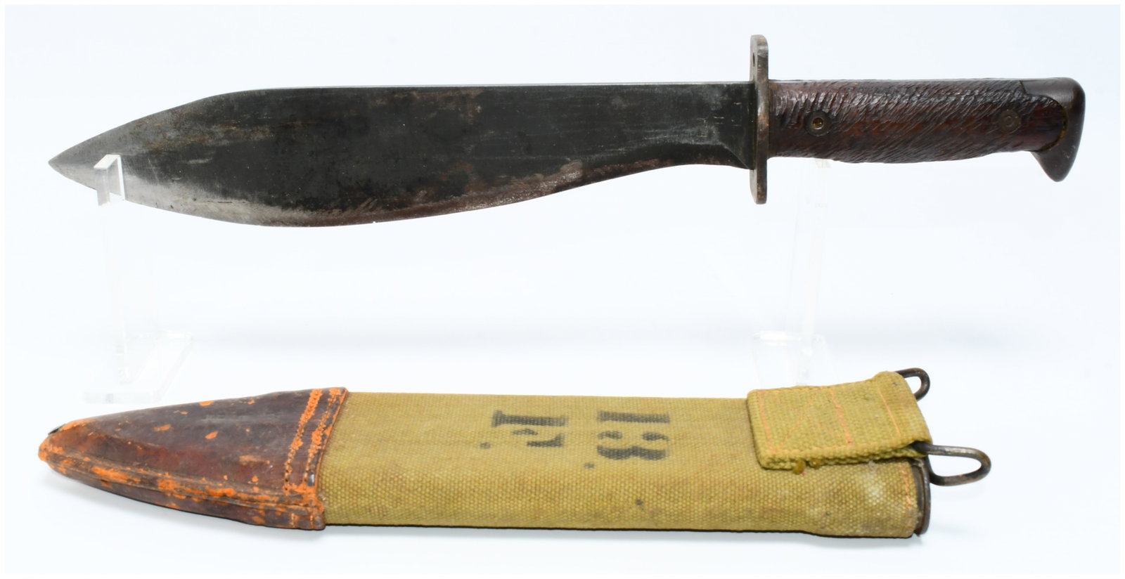 WWI US Model 1917 Bolo Knife and Scabbard: A WWI US Model 1917 Bolo Knife and Scabbard. This robust utility or fighting knife features a heavy, curved metal blade. A simple, rectangular metal crossguard separates the blade from the dark, textu