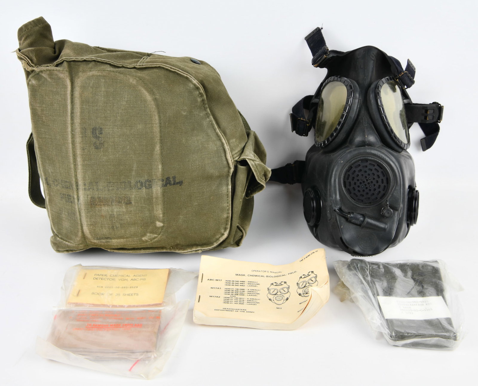 U.S. Military M17A1/M17A2 Chemical-Biological Field Mask Kit, Early 1980s: A U.S. Military M17A1/M17A2 Chemical-Biological Field Mask Kit, dating to the early 1980s. The lot comprises a black rubber gas mask with yellowed circular eye lenses and a multi-strap dark blue webbi