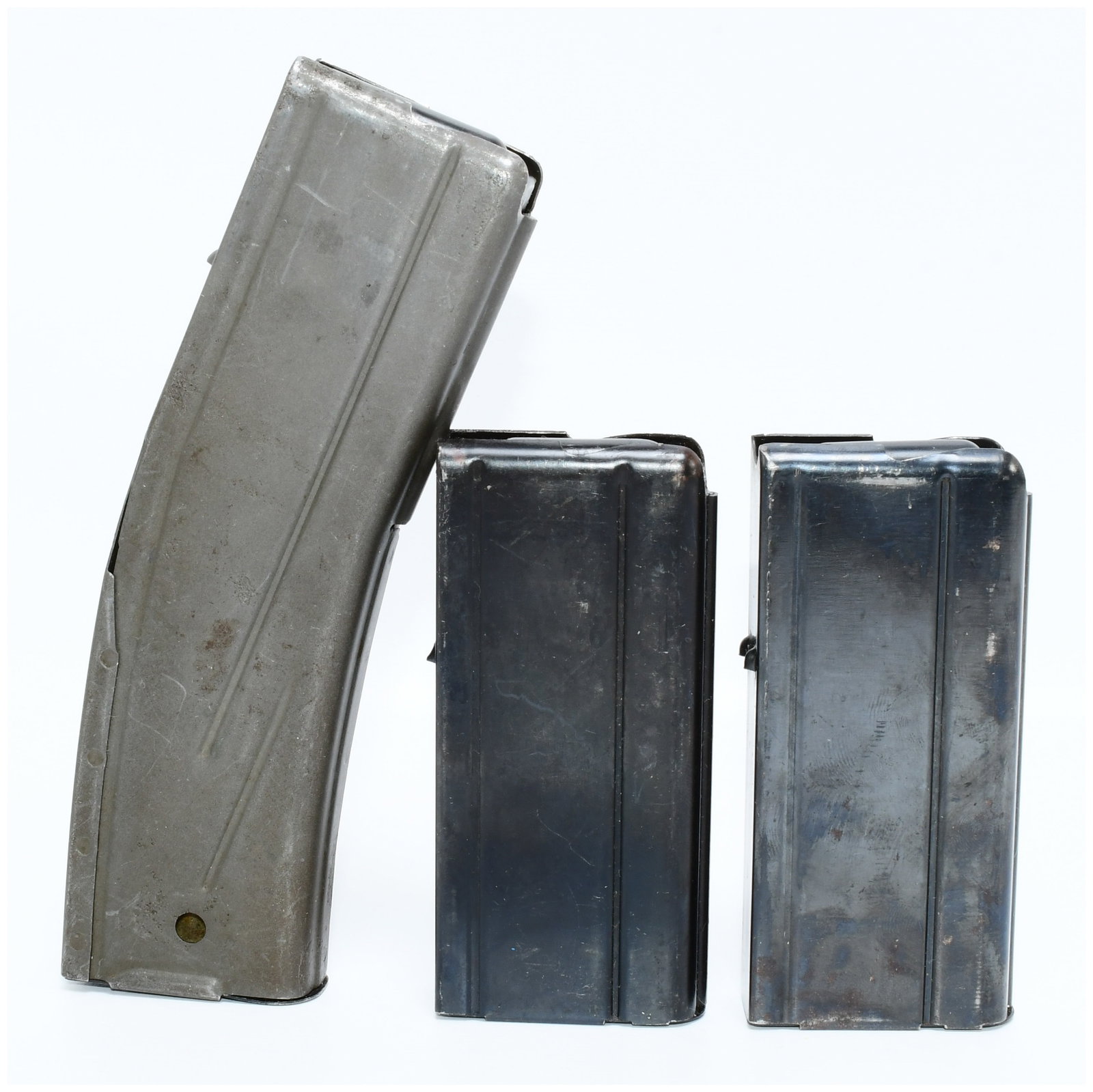 Three .30 Caliber M1 Carbine Magazines: This lot comprises three used metal firearm magazines. The largest is a curved, likely 30-round capacity magazine with a matte grey finish, featuring a faint 'U' or 'J' stamp on its spine. The other t